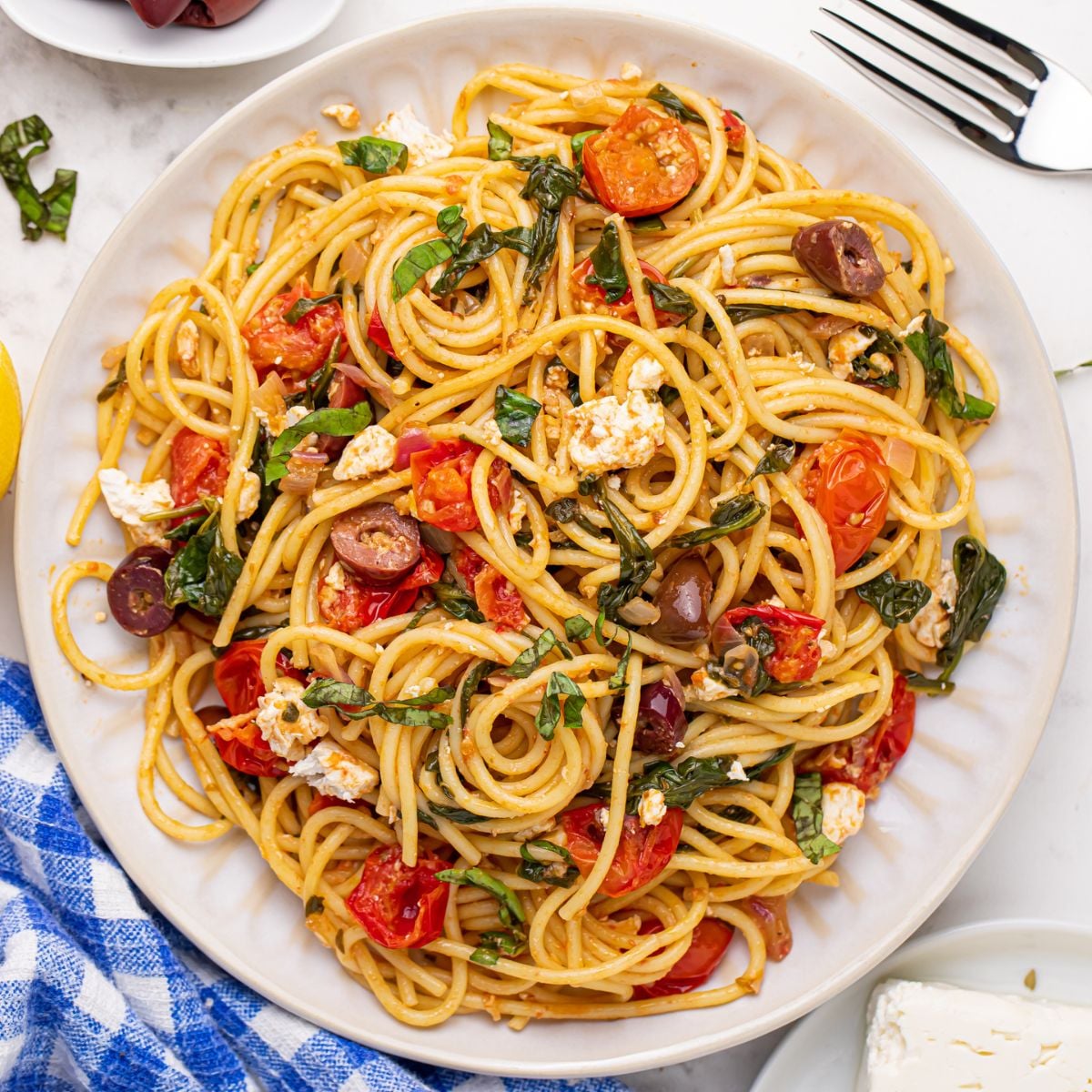 Greek Spaghetti on a plate with a fork to the side and a blue checkered towel on the side