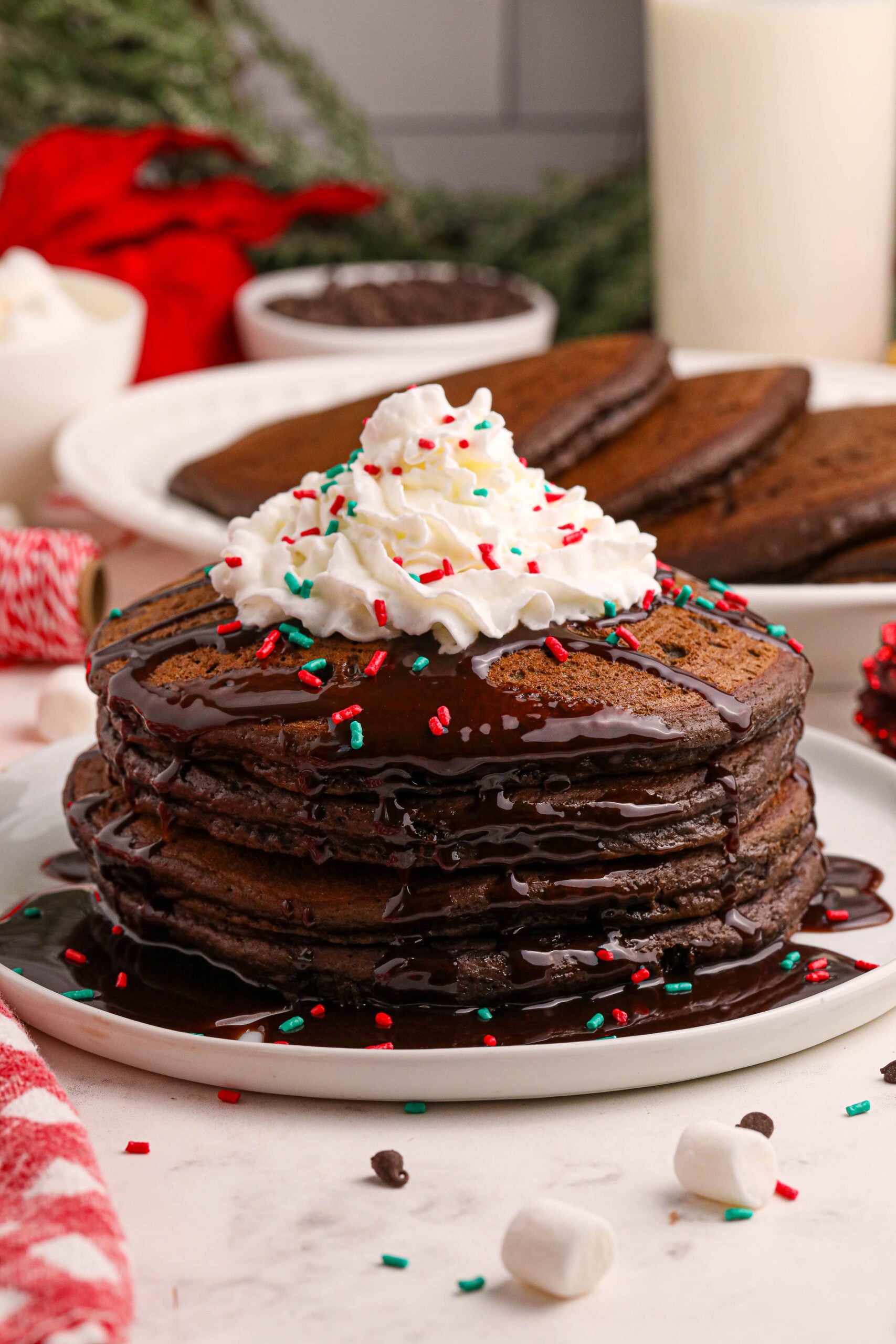Hot Chocolate Pancakes stacked on a plate topped with syrup and whipped cream and holiday sprinkles