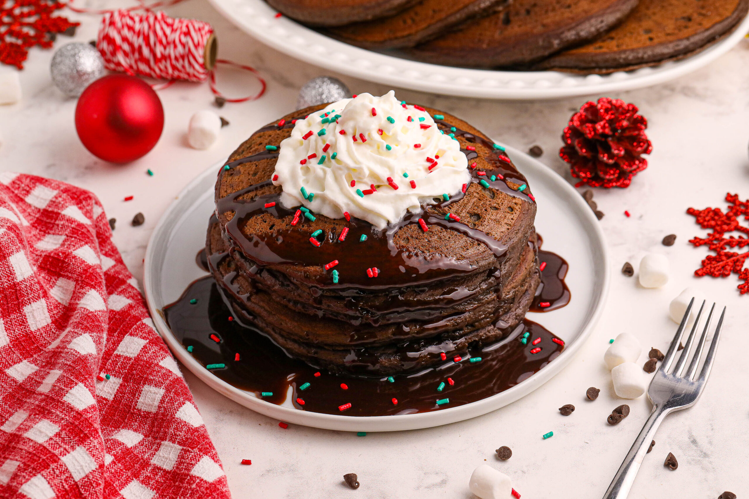 overhead shot of Hot Chocolate Pancakes stacked on a plate topped with syrup and whipped cream and holiday sprinkles
