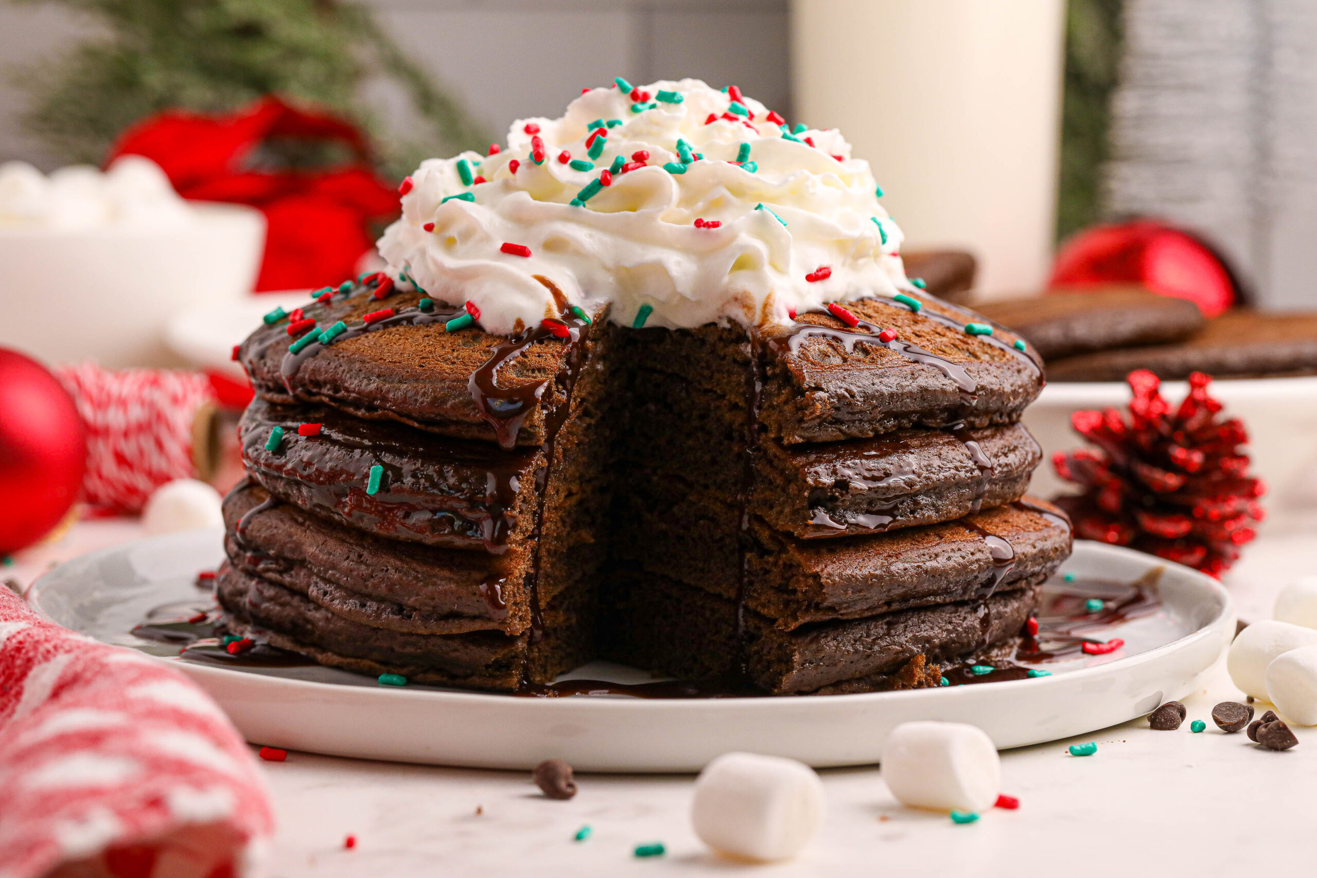 side view of Hot Chocolate Pancakes stacked on a plate topped with syrup and whipped cream and holiday sprinkles