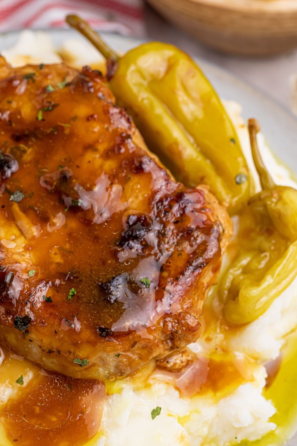 Crock Pot Mississippi Pork Chop on plate with close up view of sauce on pork chop and potatoes under and peppers on the side
