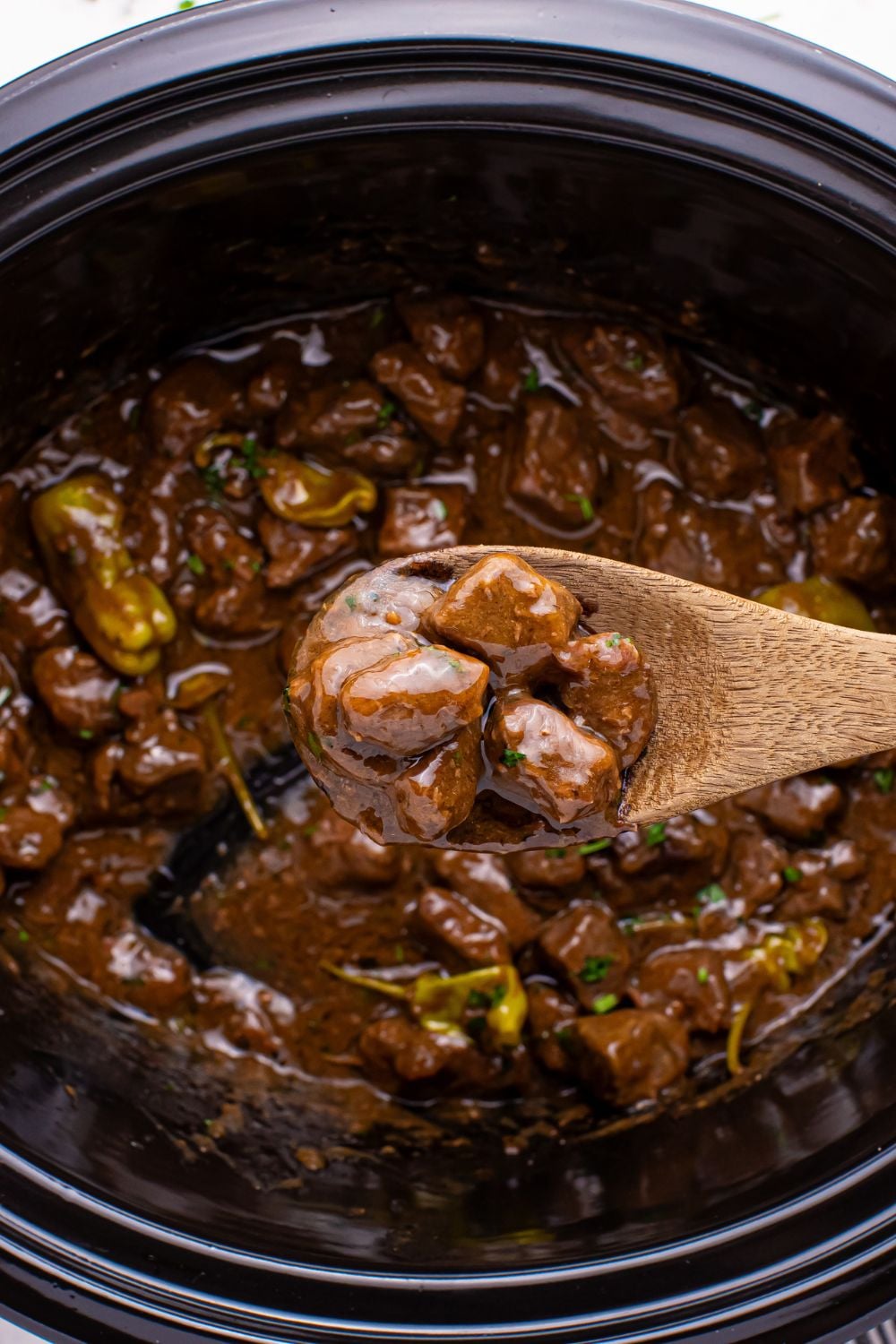 Crockpot Mississippi Steak Bites with steak bites on wooden spoon being held above crockpot