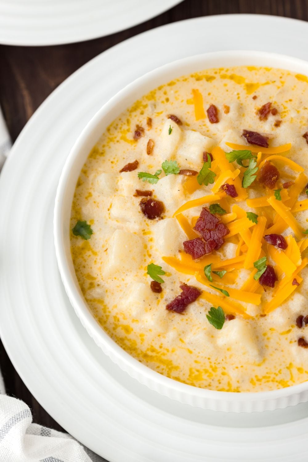 Hash Brown Potato Soup in a bowl with a white plate under it with bacon and green onions sprinkled on top of soup