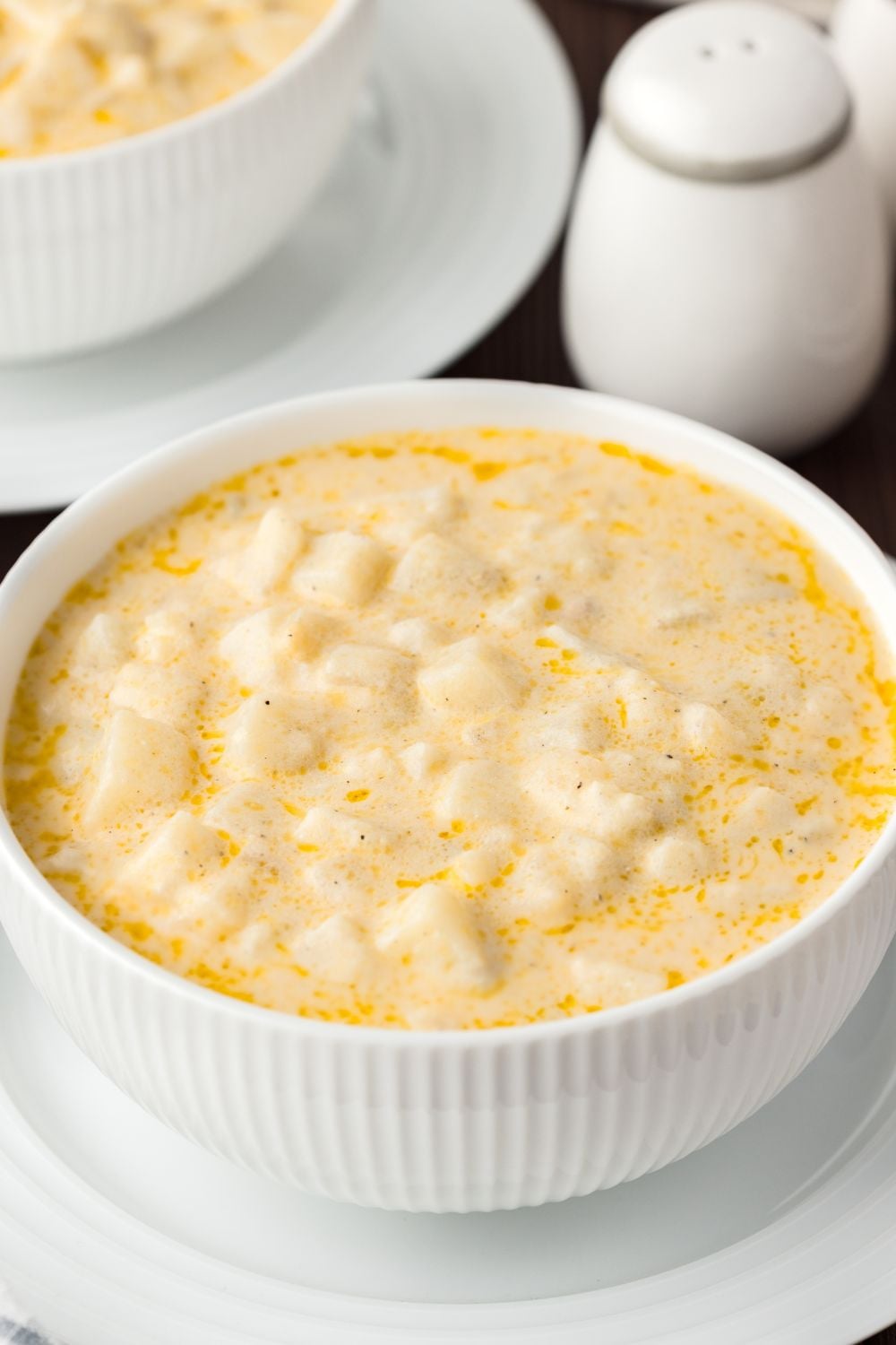 Hash Brown Potato Soup in a bowl with white dishes around the soup
