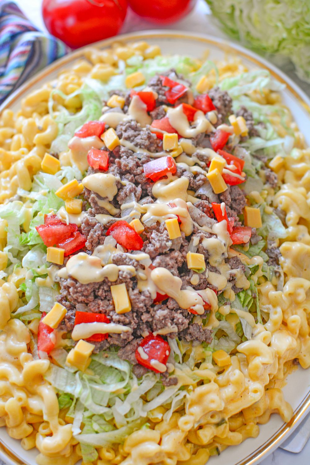 Big Mac Macaroni And Cheese on a platter with tomatoes and towel behind the platter