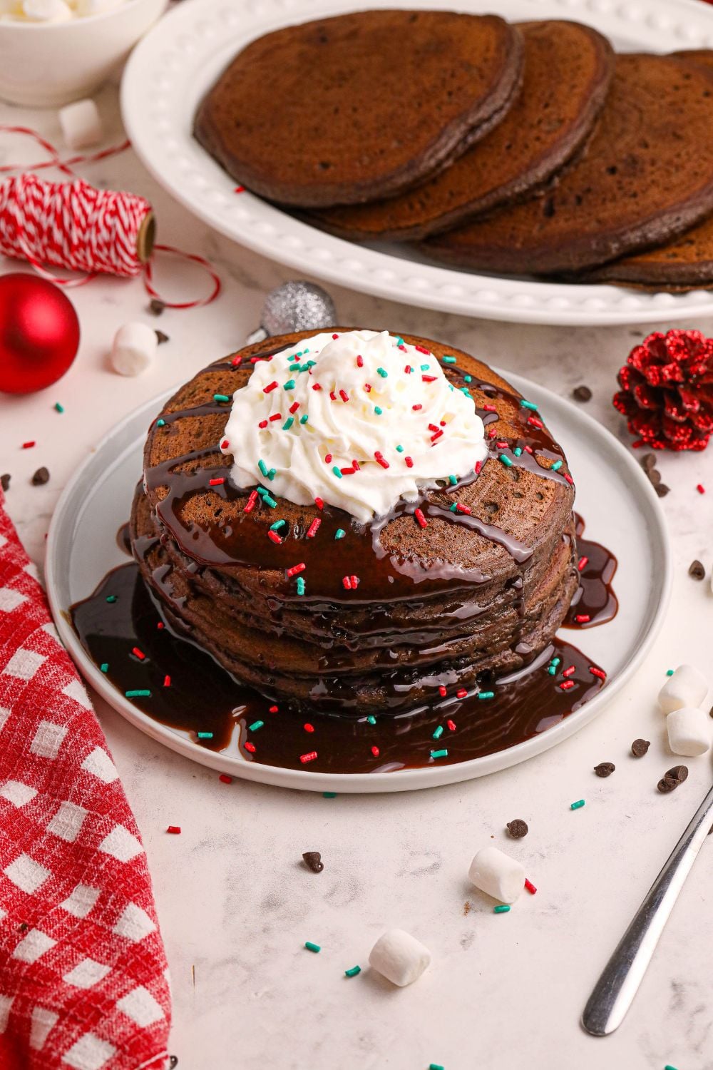 Hot Chocolate Pancakes on plate with whipped cream and a stack of pancakes spread on a platter in background