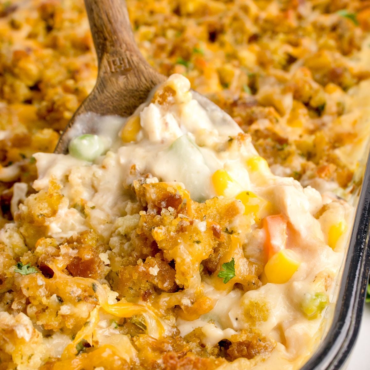 Chicken Stuffing Casserole in a pan with a wooden spoon scooping some of the casserole out of the pan