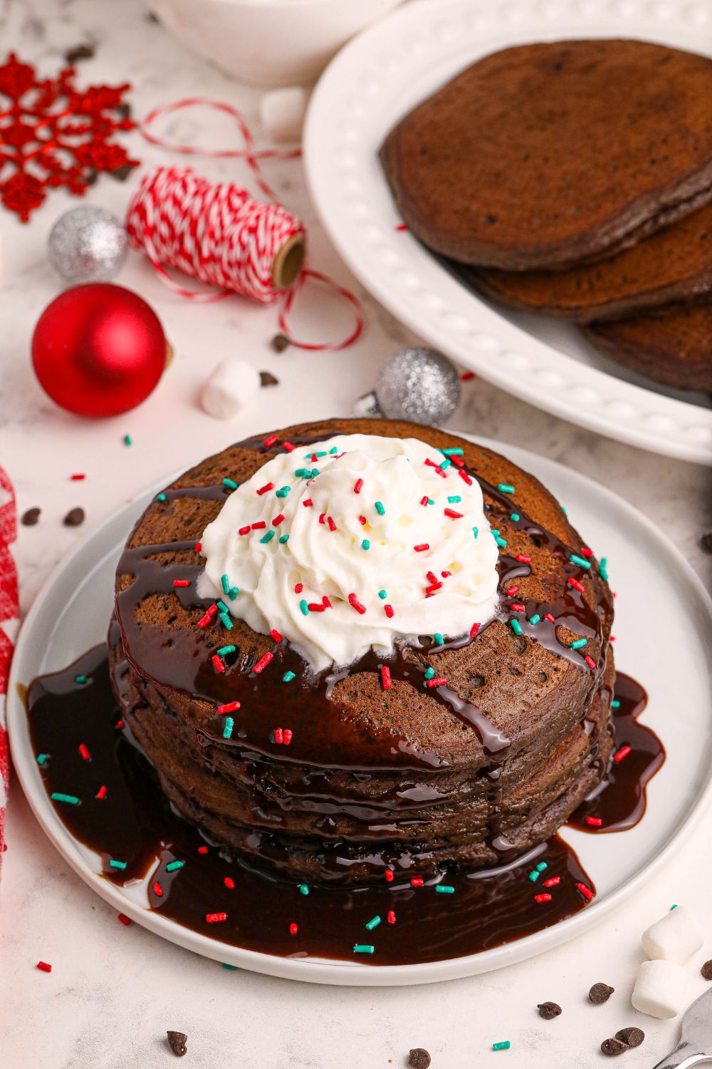 Hot Chocolate Pancakes with whipped cream on plate with christmas decor behind it