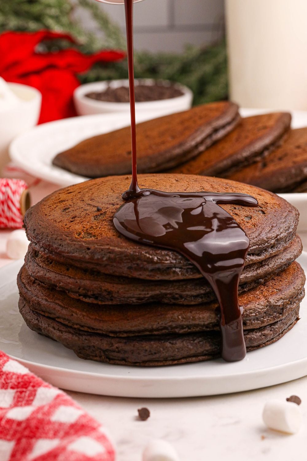 Hot Chocolate Pancakes stacked on plate with chocolate syrup pouring over the pancakes