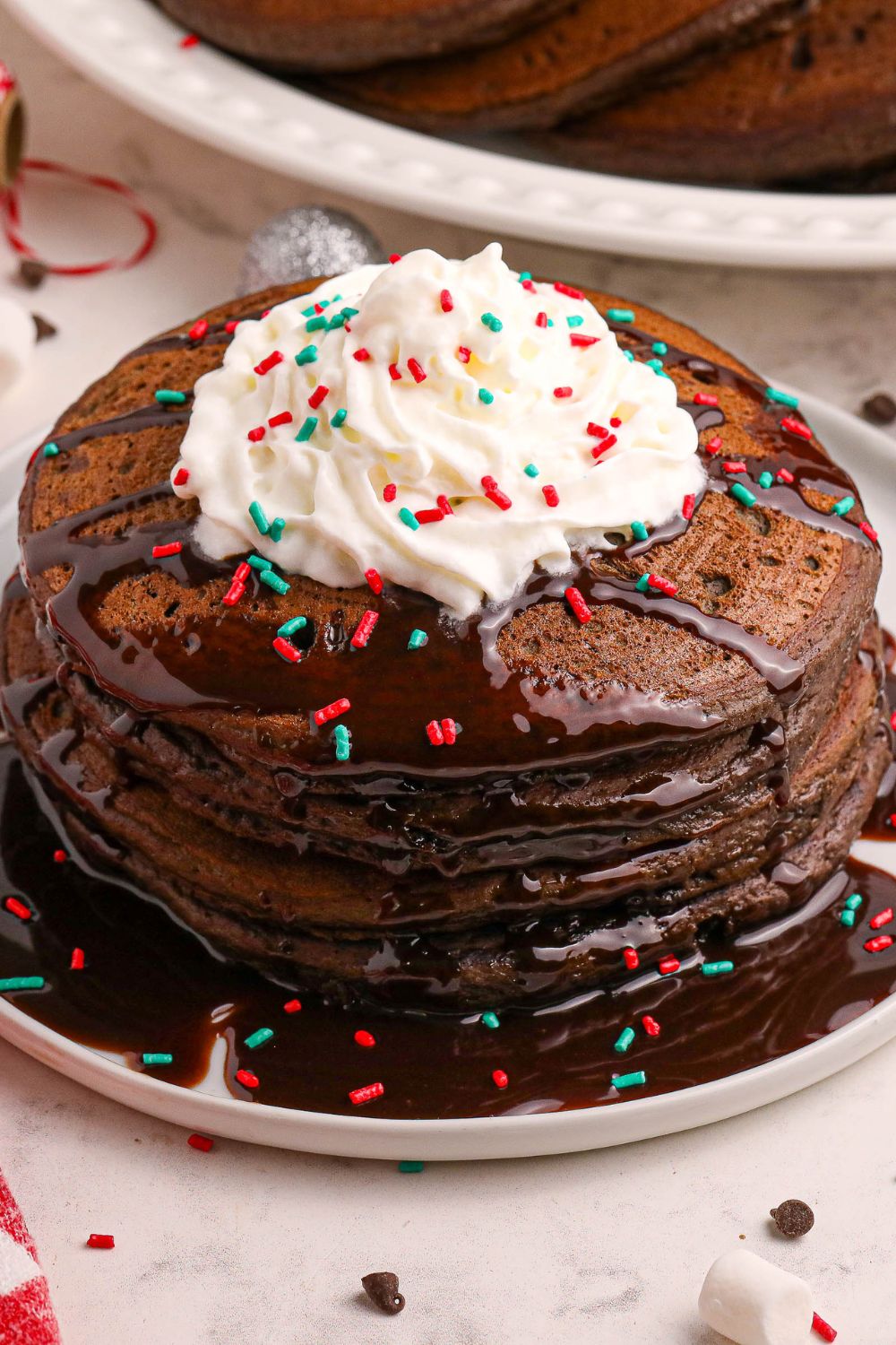 Hot Chocolate Pancakes stacked on a plate with hot chocolate and whipped cream and festive sprinkles