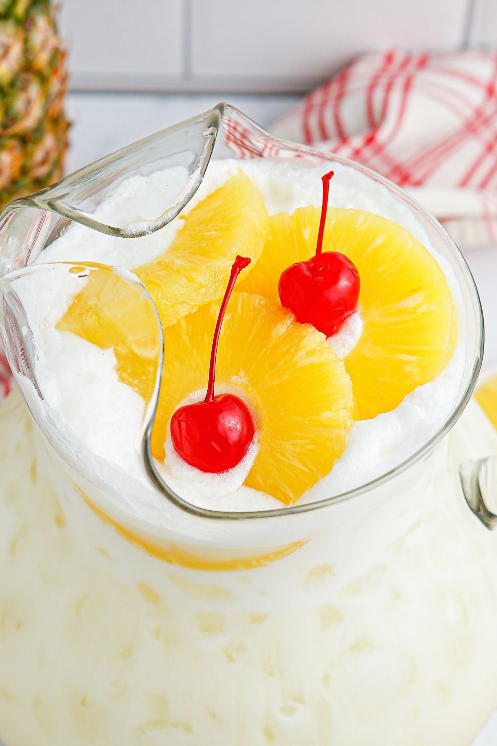 Pina Colada Punch in a pticher with a close up of pineapple slices and cherries sitting on top of punch