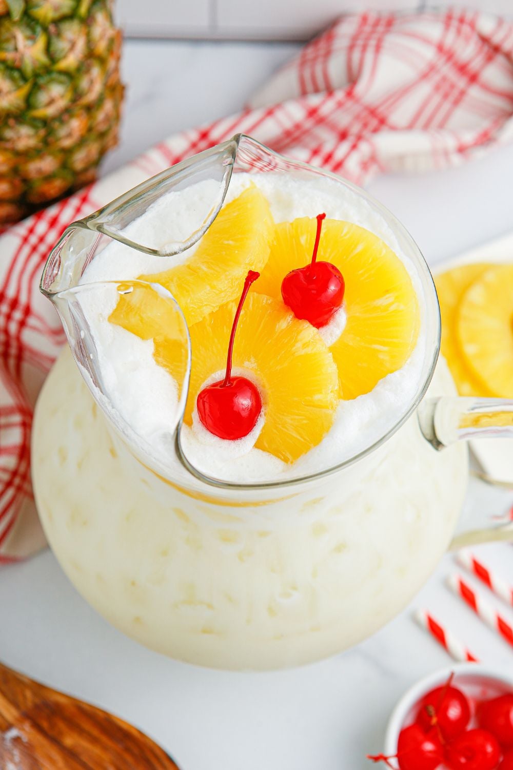 Pina Colada Punch in a pitcher on table with pineapple and cherry on top of punch 