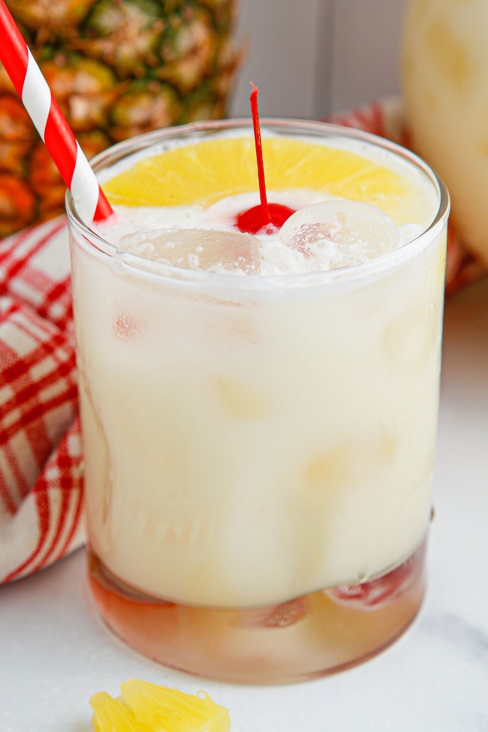 Pina Colada Punch in a small glass with cherry and slice of pineapple on top wit a red straw stuck in glass 