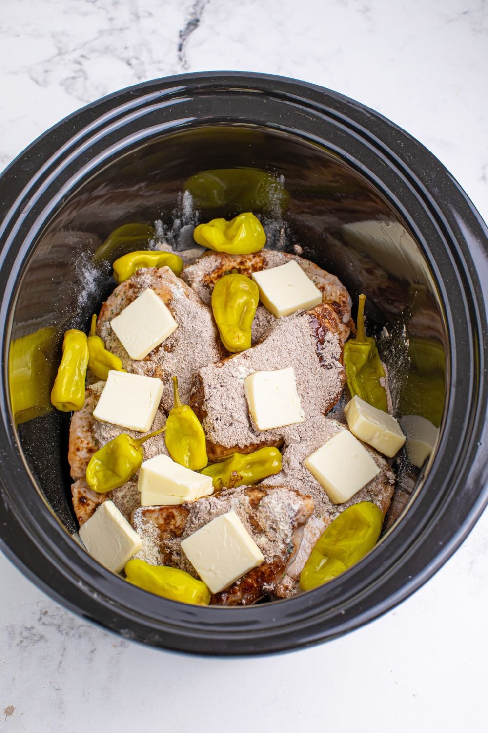 Crock Pot Mississippi Pork Chops ingredients in a slow cooker with slabs of butter on top
