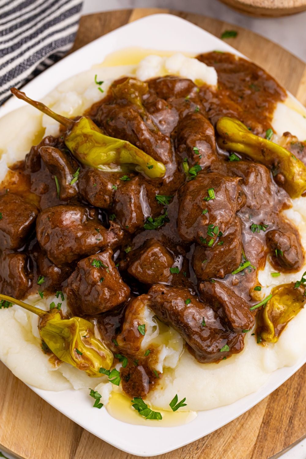 Crockpot Mississippi Steak Bites on a square plate with peppers and meat on it