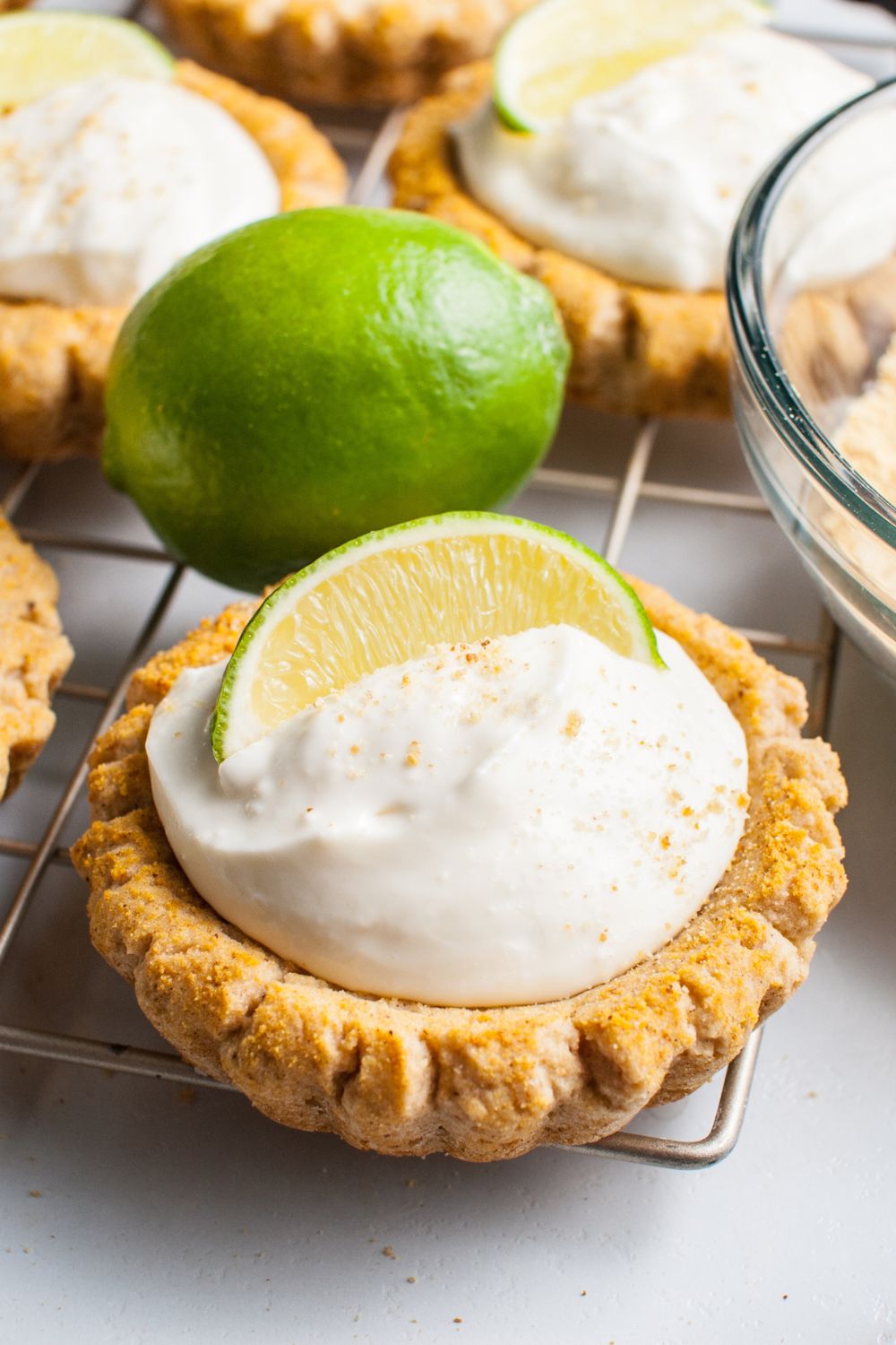 Crumbl Key Lime Pie Cookies on a wire cooling rack with a lime wedge on each cookies and then a full lime on table