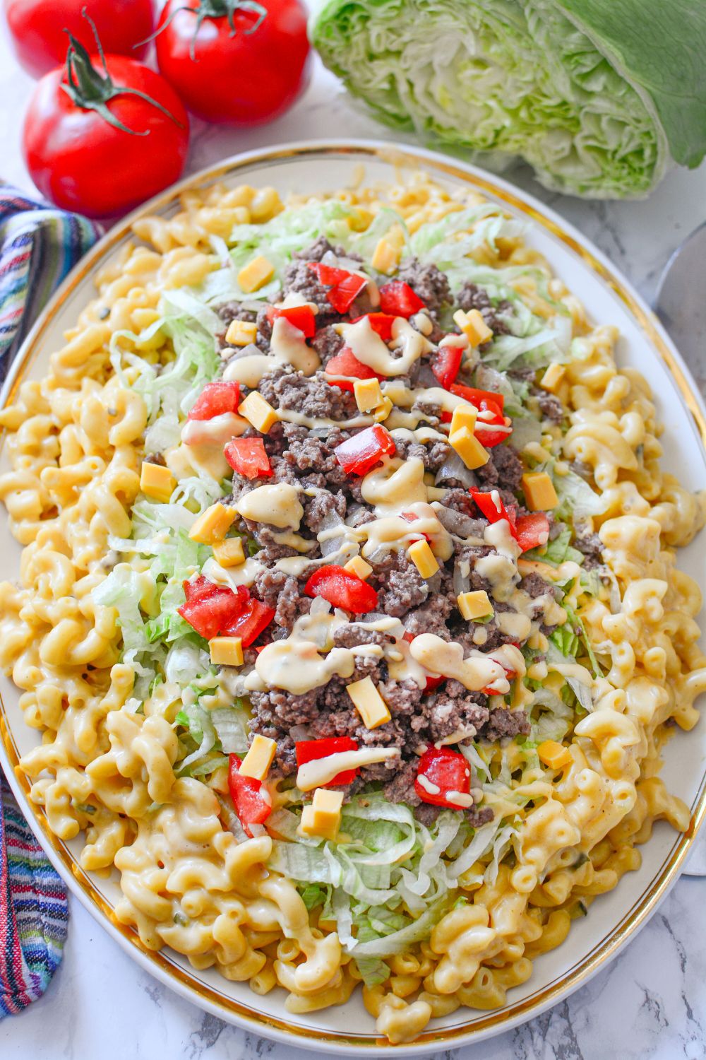 Big Mac Macaroni And Cheese in an oval platter with tomatoes and lettuce around it on table