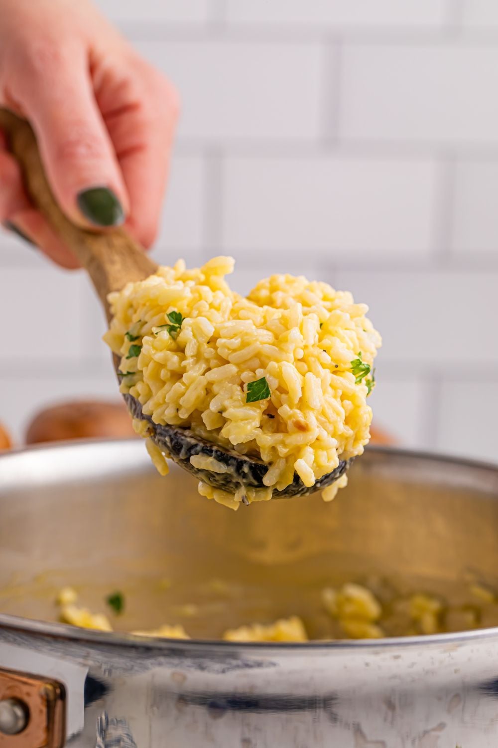 Souper Rice in a plastic spoon being held in a hand above metal pan full of rice