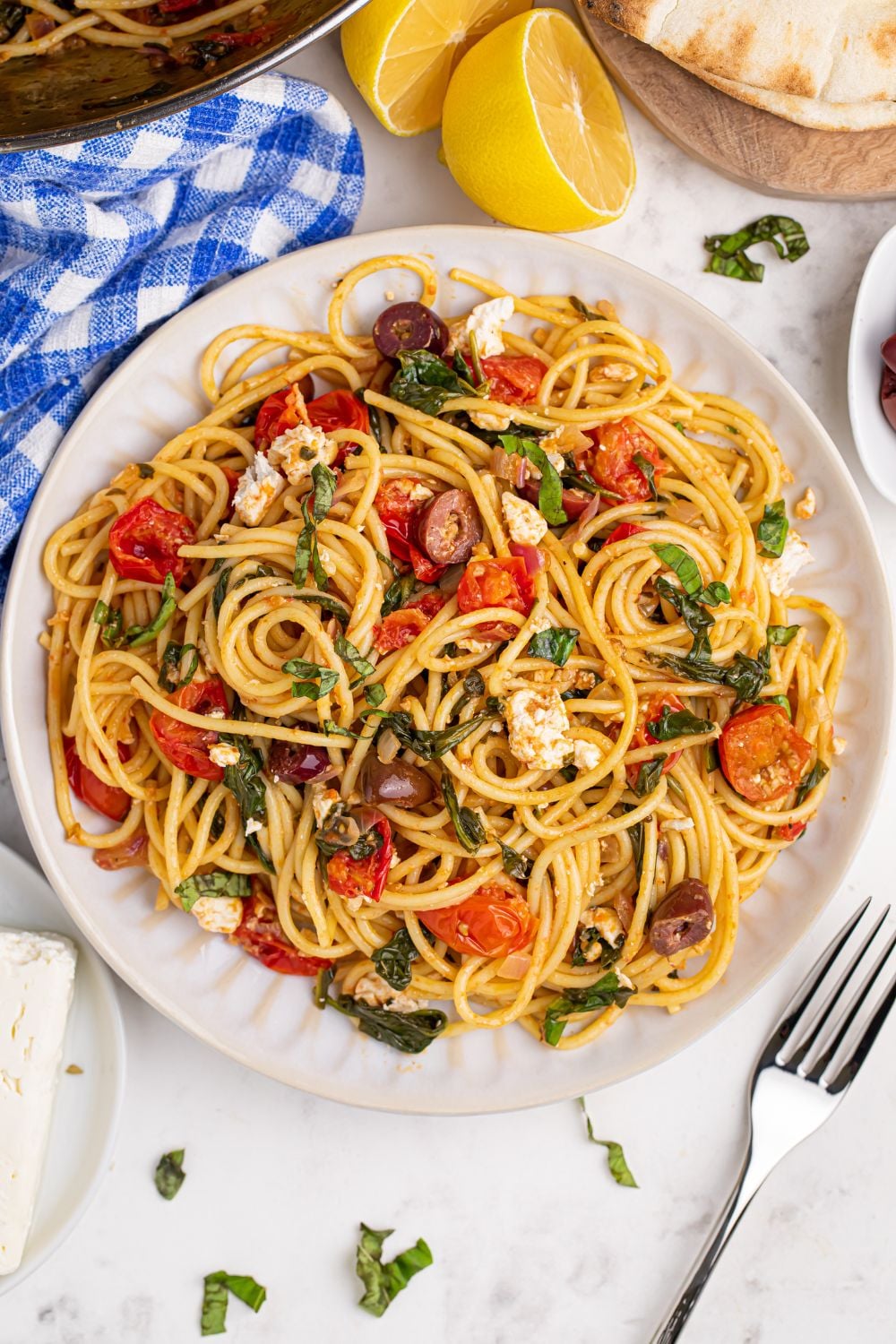 Greek Spaghetti on a plate iwth a towel and fork on table near the plate and lemon wedges around the plate 