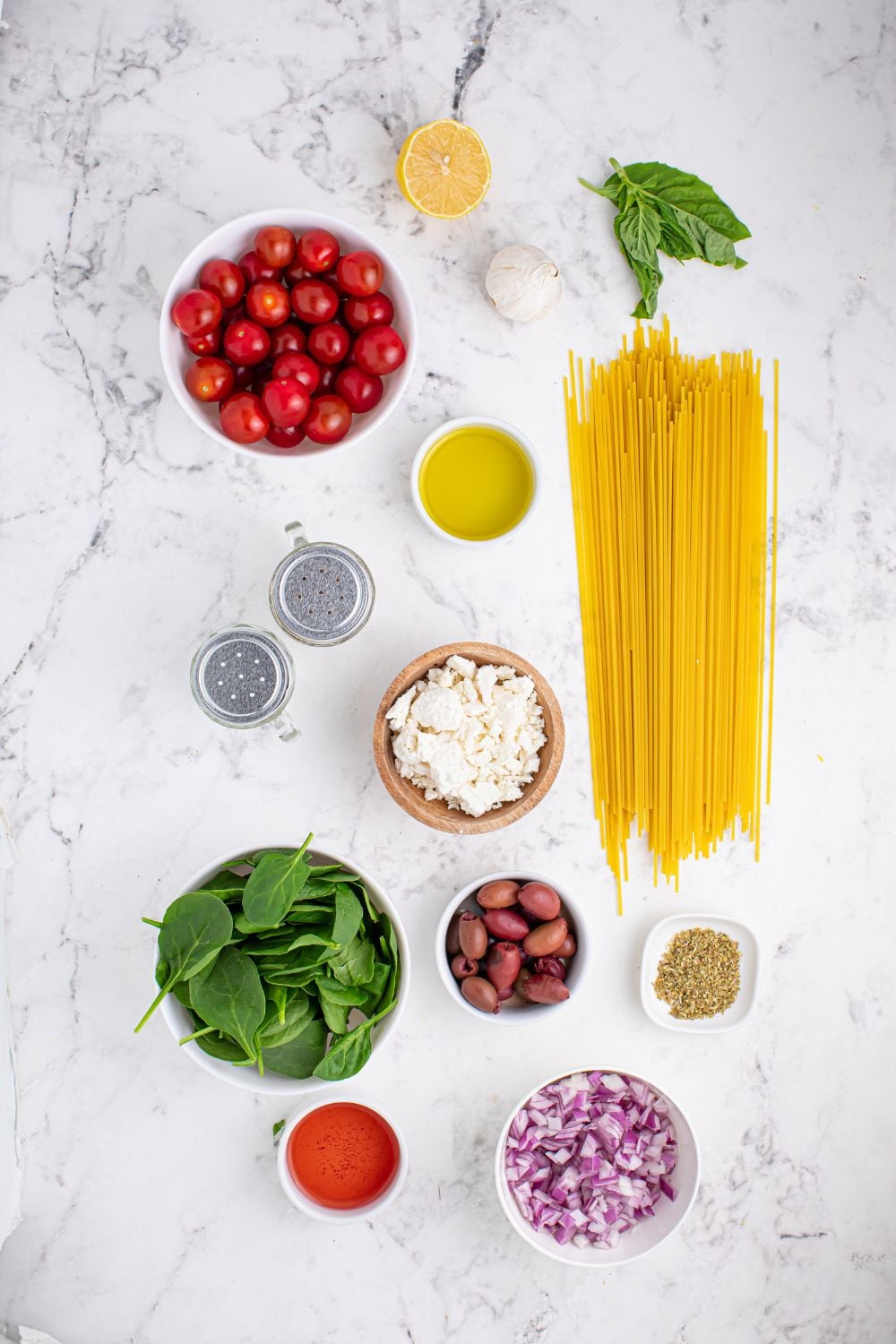 Greek Spaghetti ingredients on a marble countertop. Each ingredient is in its own bowls 