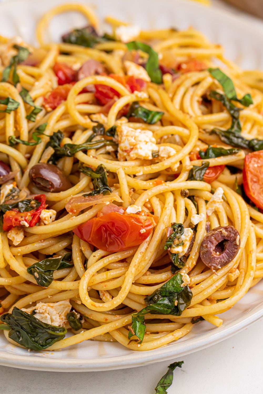 Greek Spaghetti on a plate with tomatoes, olives, feta cheese and more mixed in the pasta