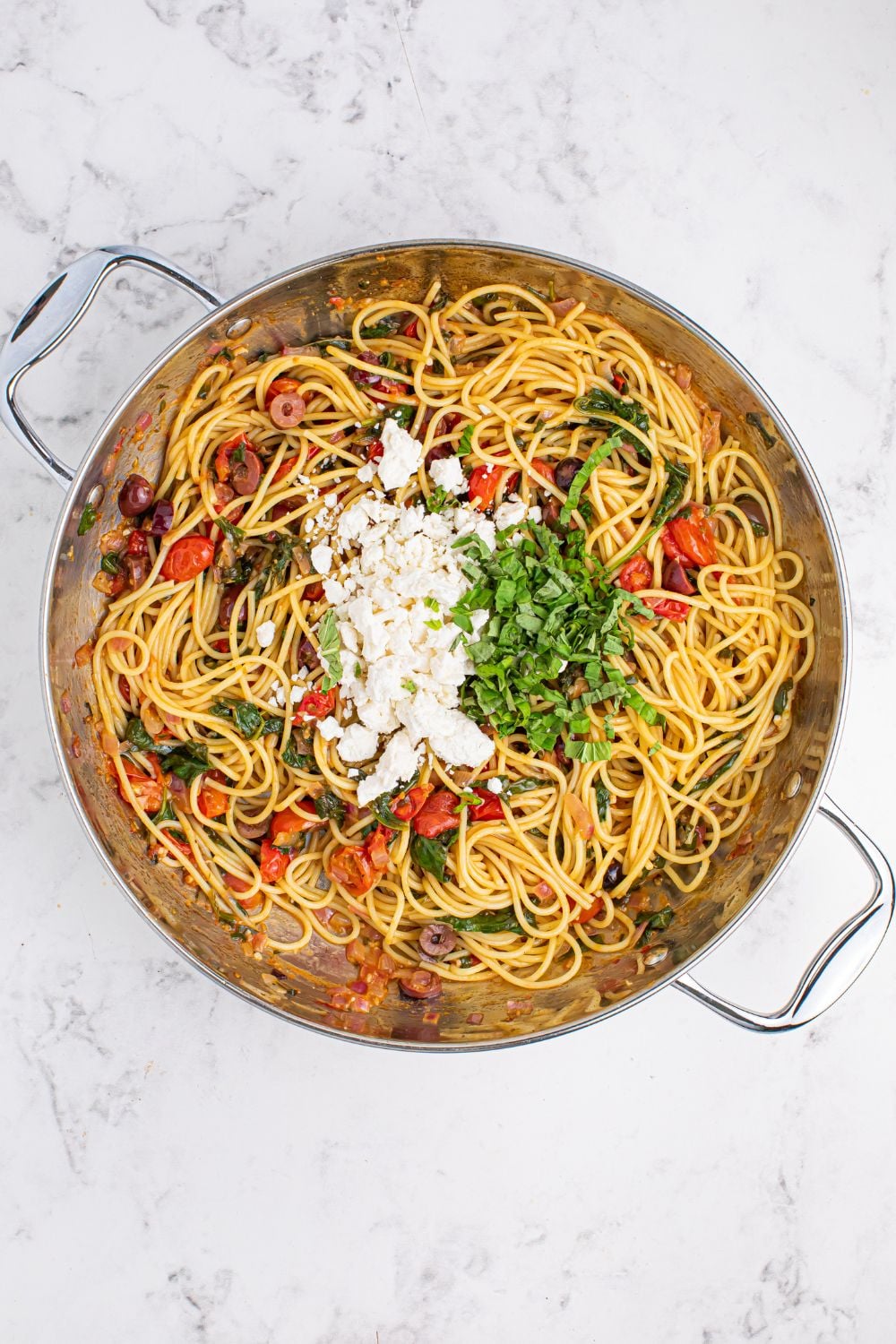 Greek Spaghetti ingredients in a pan with feta and basil on top 
