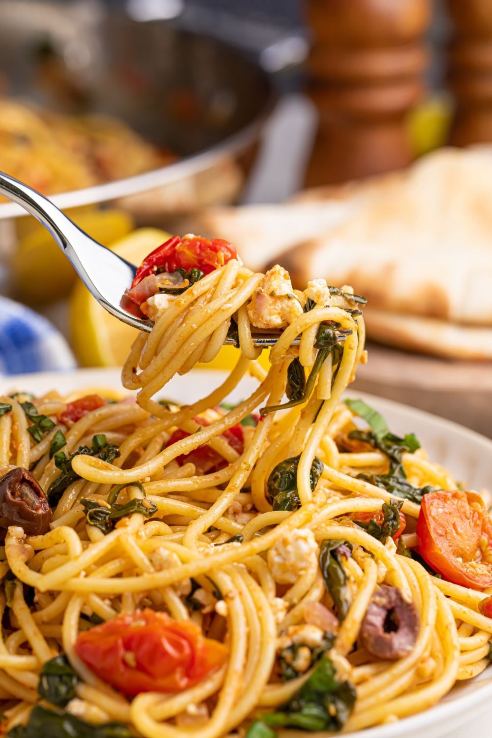 Greek Spaghetti on fork being lifted up above the plate on table with salt and pepper shaker in the background 