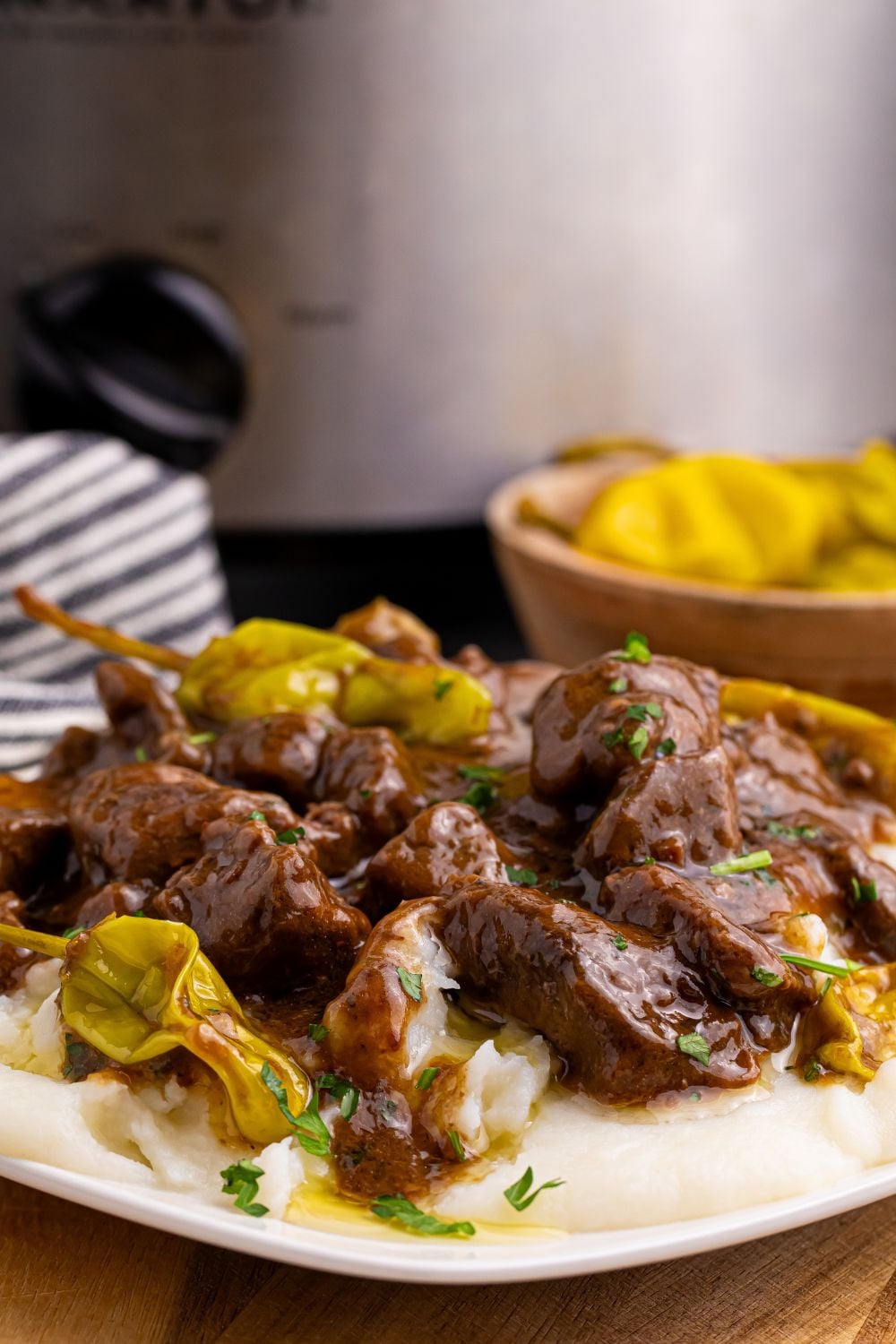 Crockpot Mississippi Steak Bites on plate with slow cooker in back
