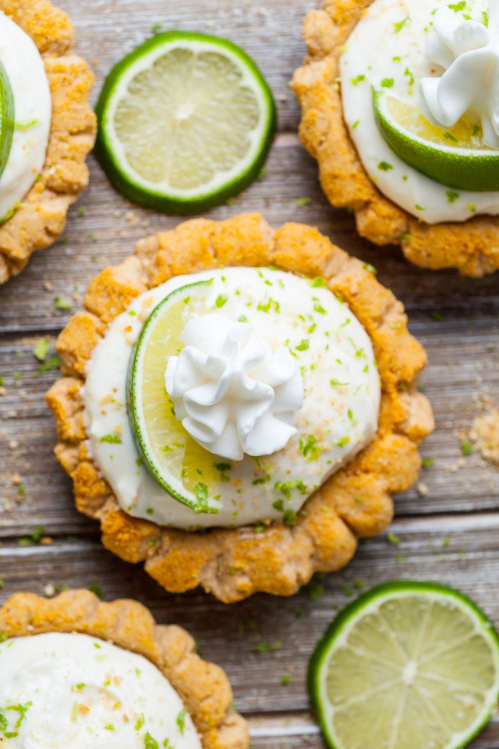 Crumbl Key Lime Pie Cookies spread out on a wooden table with lime slices around the cookies