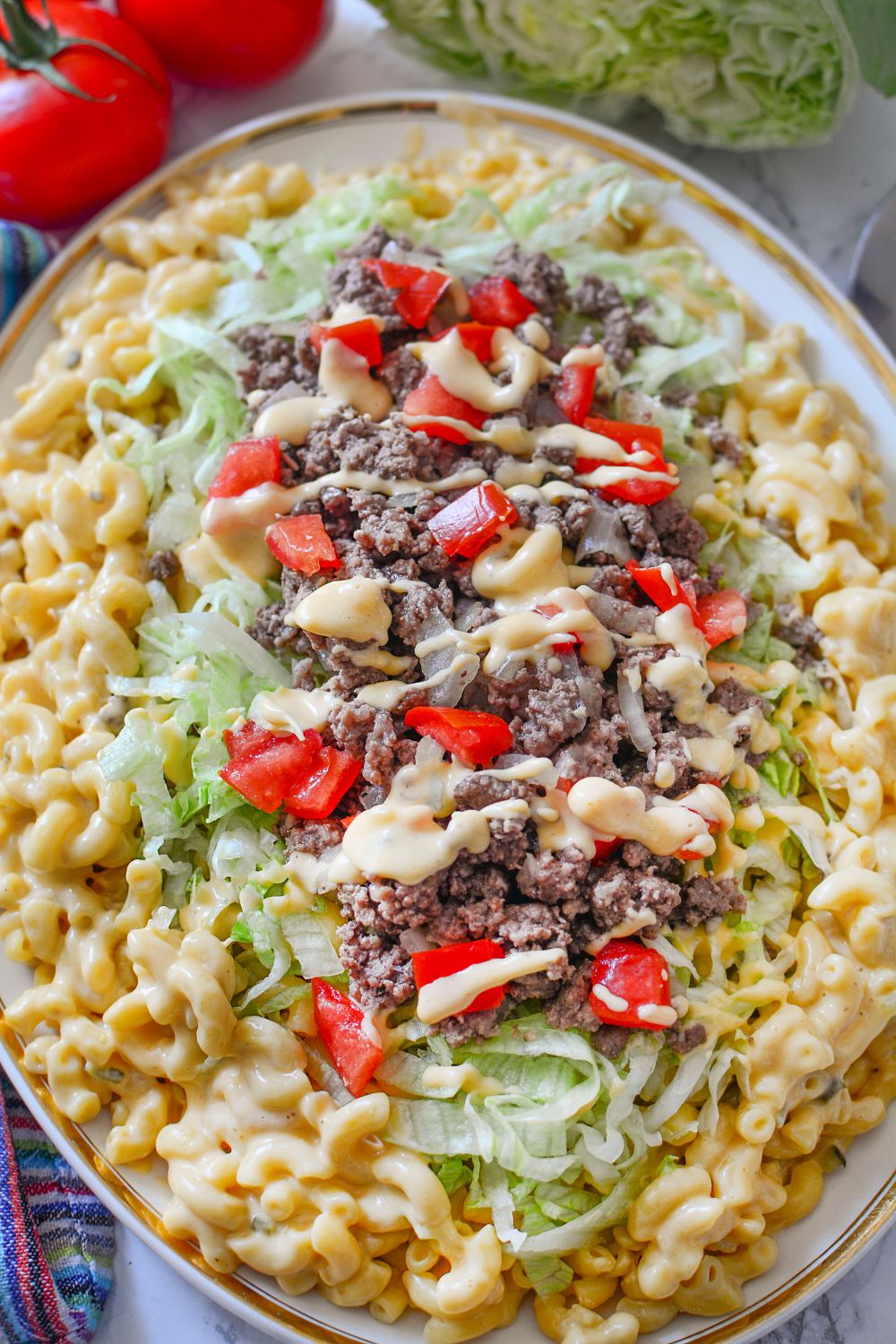 Big Mac Macaroni And Cheese on a platter on table with some tomatoes and lettuce in background