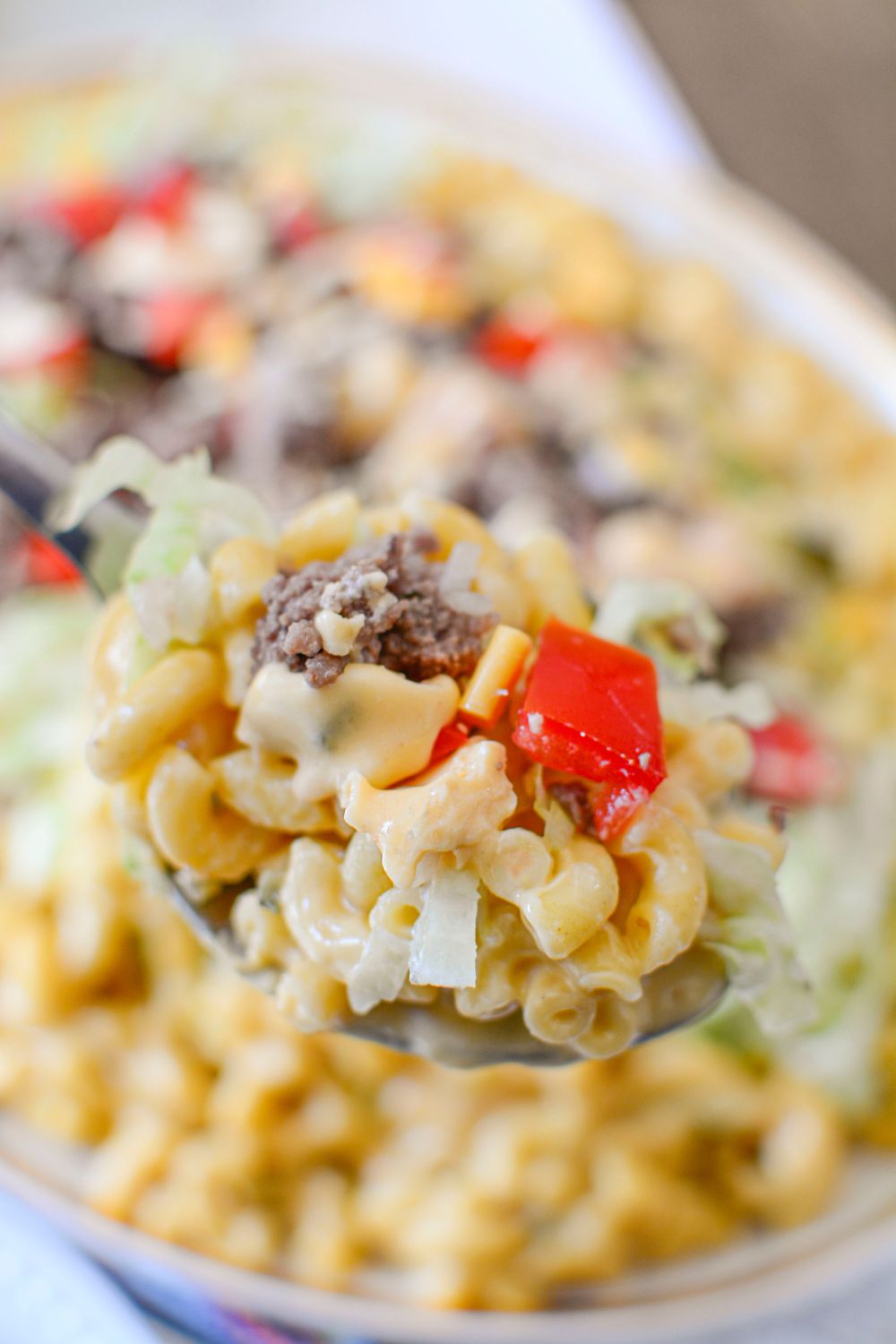 Big Mac Macaroni And Cheese on a spoon above the plate full of mixture that is sitting on table