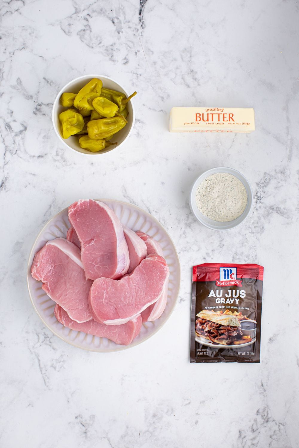 Crock Pot Mississippi Pork Chops ingredients on table - pork chops, au jus packet, ranch seasoning, stick of butter, peppers