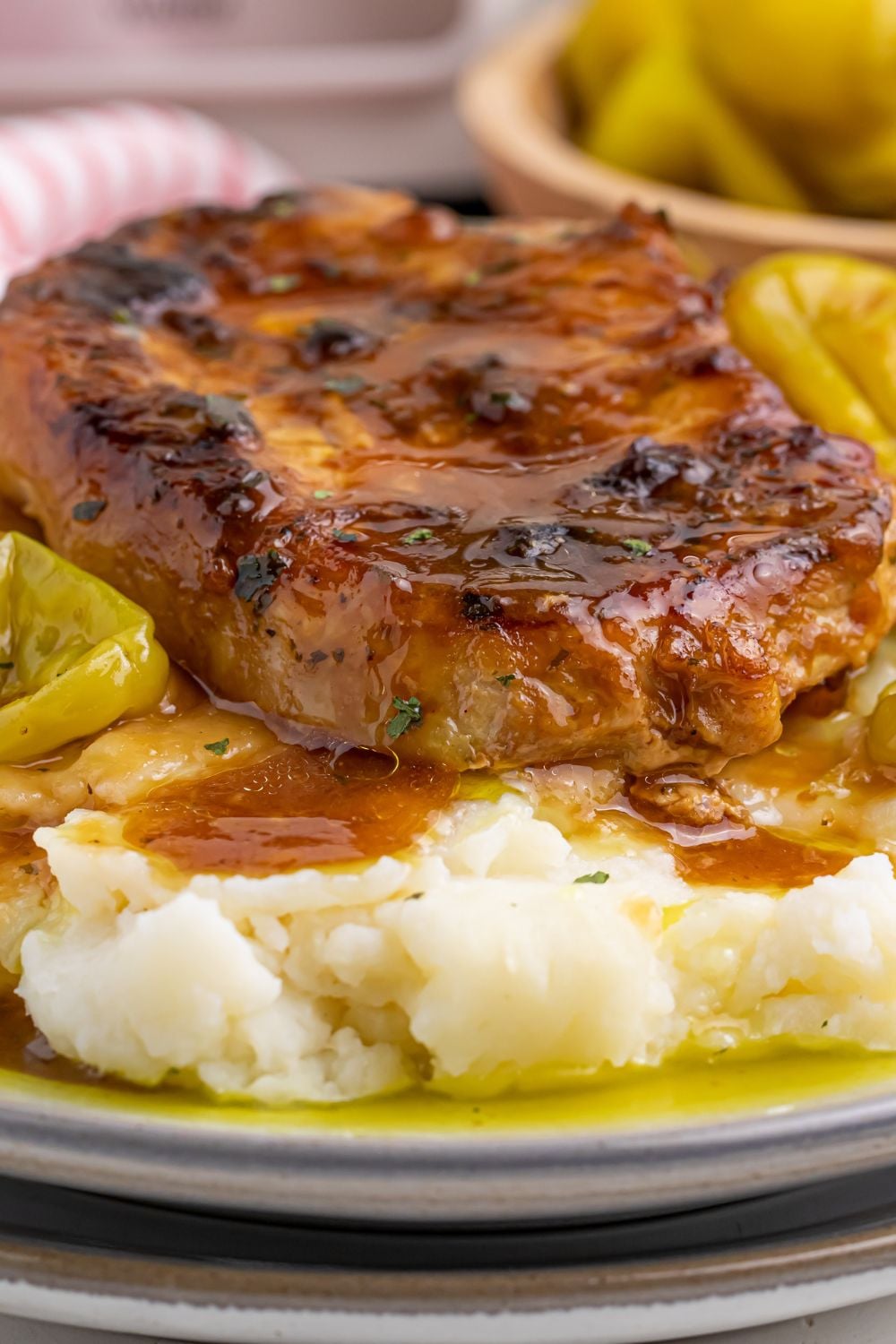 Crock Pot Mississippi Pork Chop on a plate with bed of mashed potatoes with peppers in a bowl on the side of plate