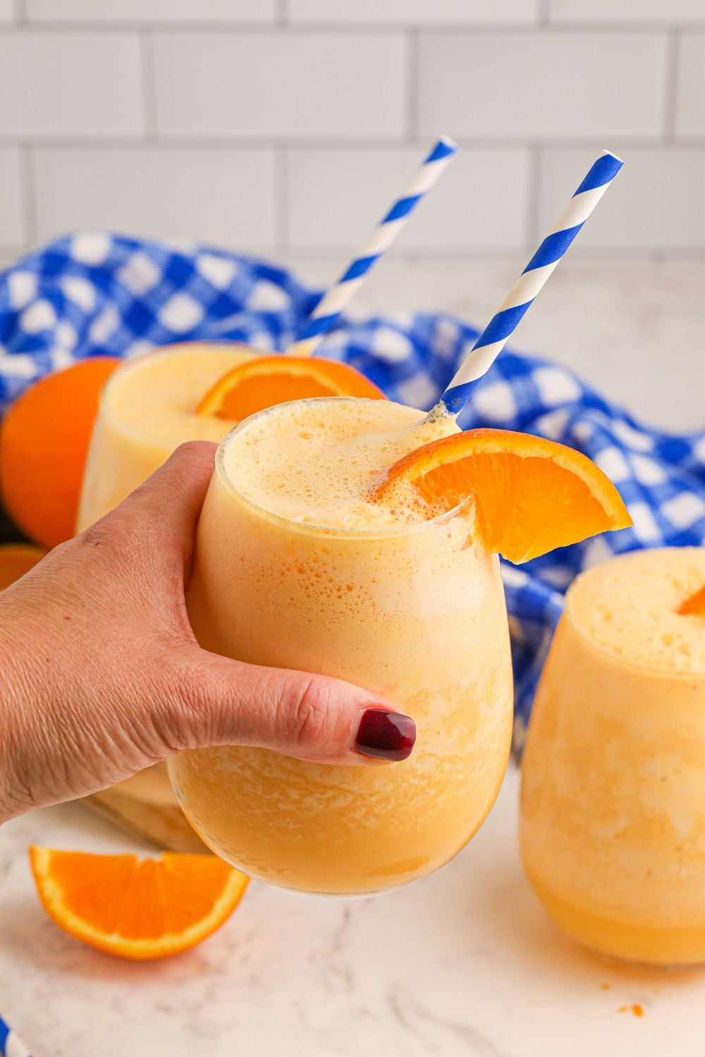 Copycat Orange Julius in hand and two more glasses of Julius on table with orange wedges around it