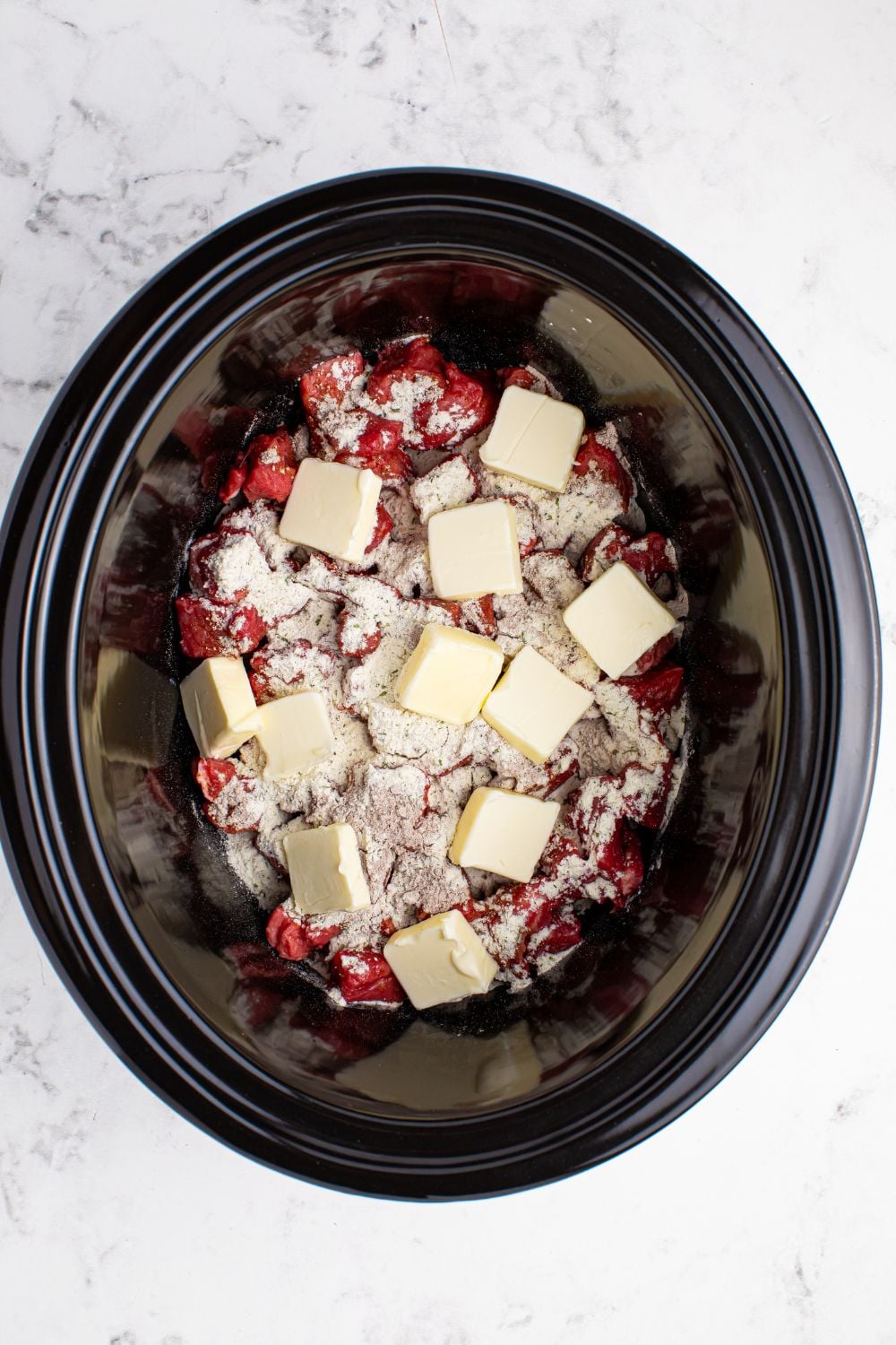 Crockpot Mississippi Steak Bites with diced steak and dry seasoning sprinkled on top of meat and cubes of butter on top