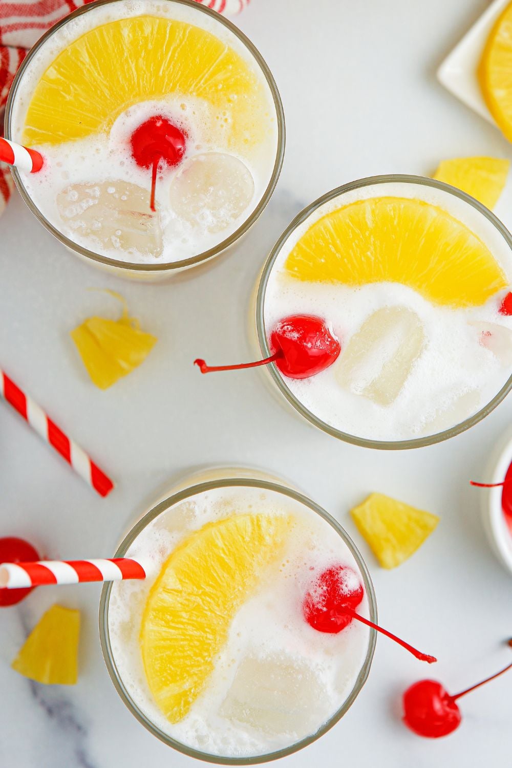 Pina Colada Punch in glasses on table topped with some pineapple and cherry in each glass 