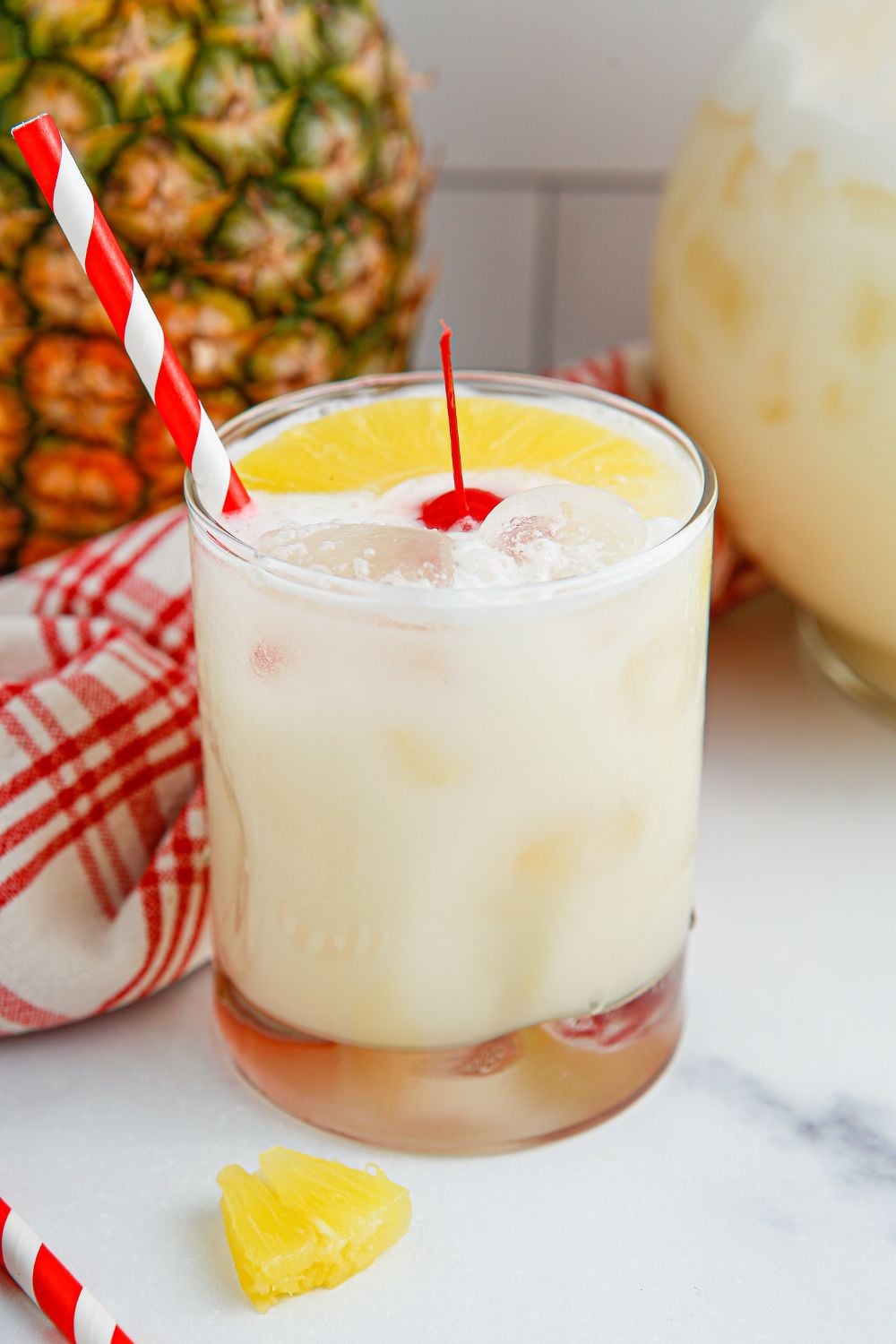 Pina Colada Punch sitting on table in a glass with a pineapple and pitcher of punch in behind the glass 