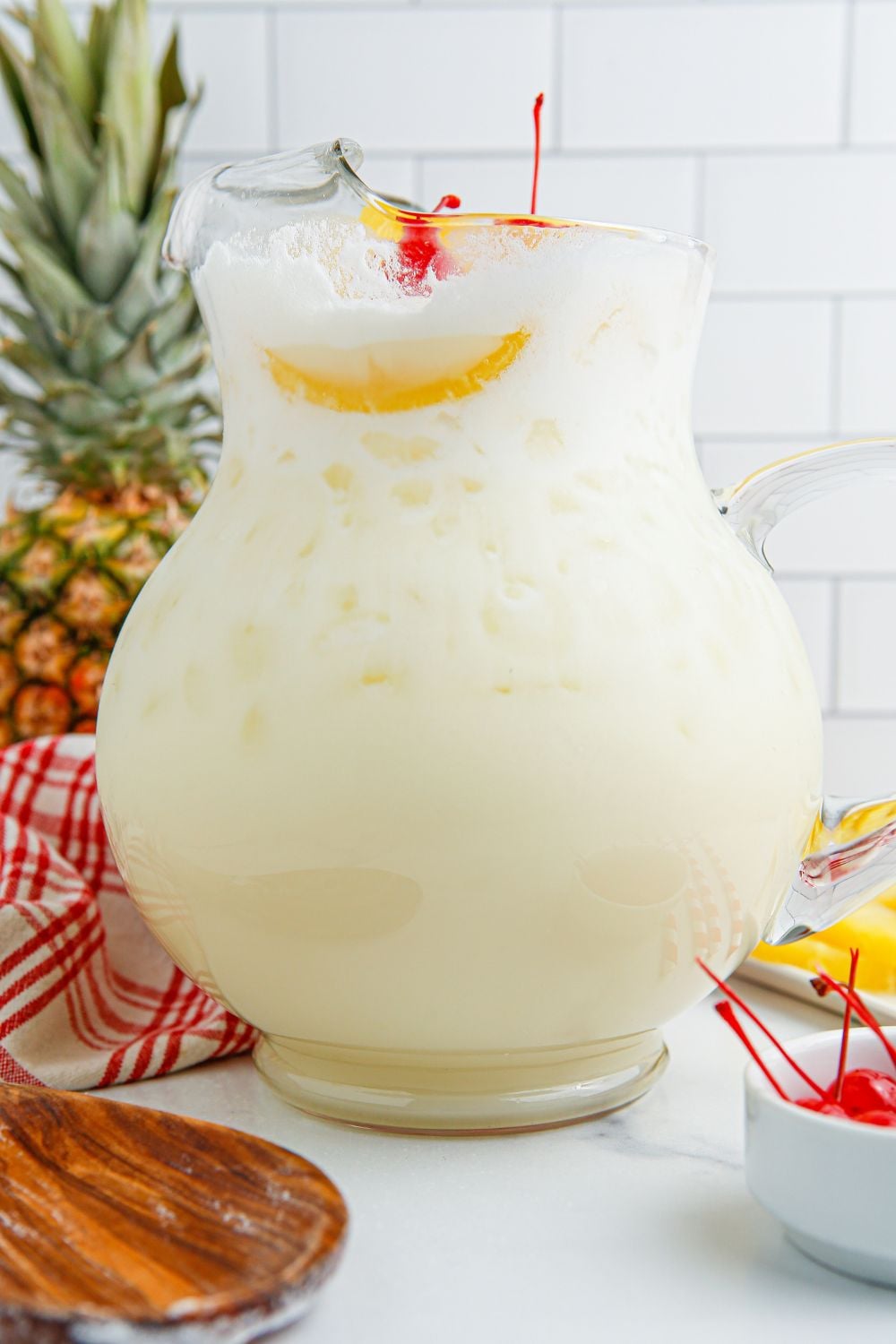 Pina Colada Punch in a pitcher with a pineapple and bowl of cherries in a bowl 