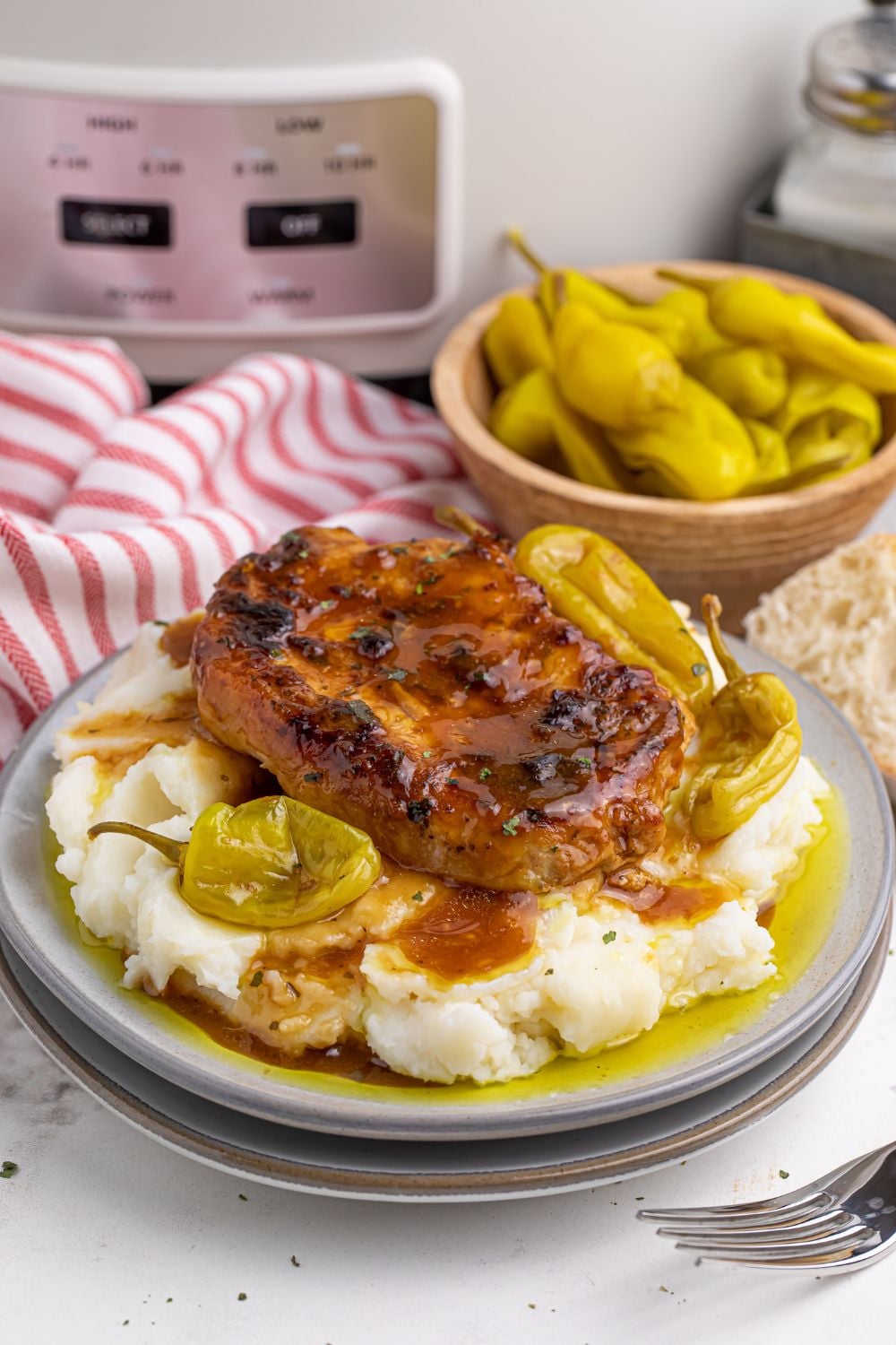 Crock Pot Mississippi Pork Chops on plate with a bowl of peppers in background and a crockpot