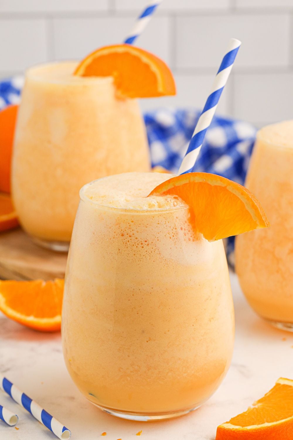 Copycat Orange Julius drinks spread out on table with orange wedge on side of glass and blue and white striped straws