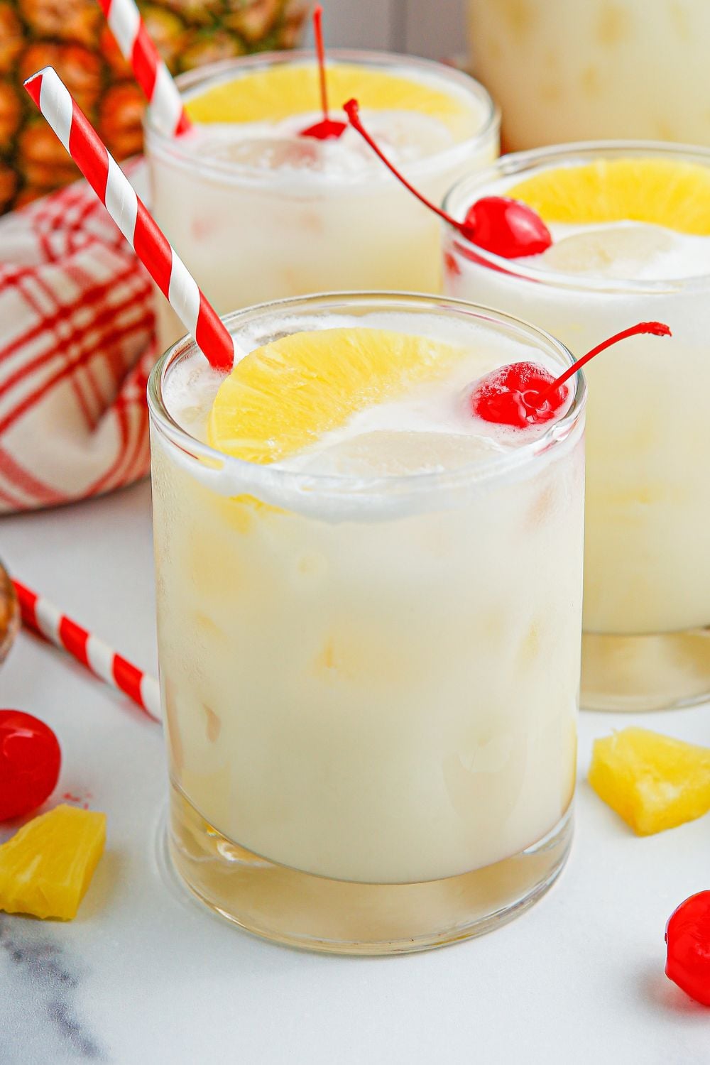 Pina Colada Punch in three glasses sitting on table with garnishes on top and placed around the glasses 