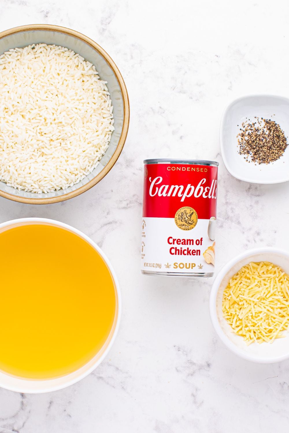 Souper Rice ingredients in glass bowls - rice, chicken stock, black pepper cheese, and a can of condensed soup in the center of the bowls displayed on table