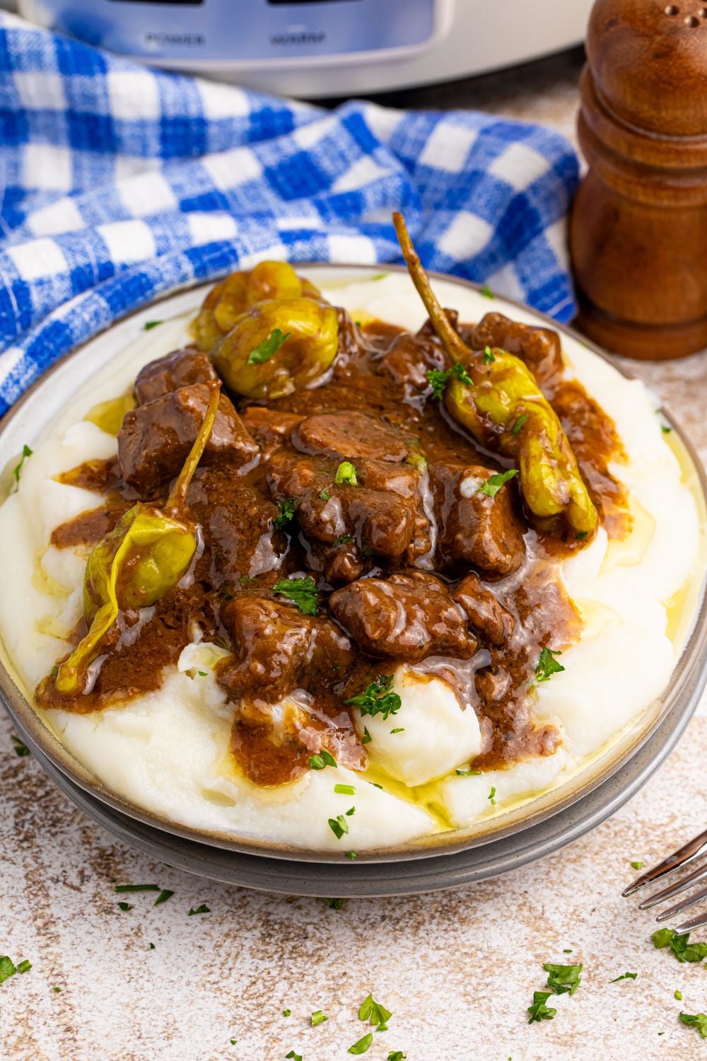 Crockpot Mississippi Steak Bites on plate with a blue check towel behind it