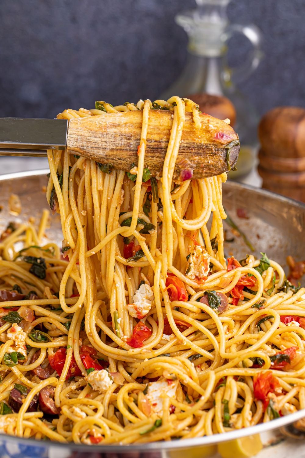 Greek Spaghetti using tons to lift some of the pasta and veggies out of the pan 