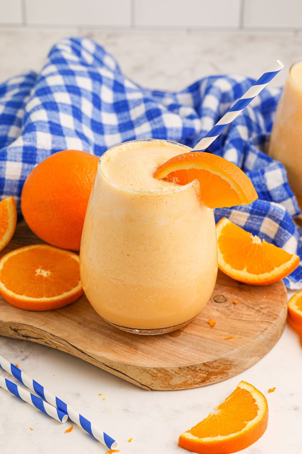 Copycat Orange Julius on table with oranges and slices around it and a blue and white checked towel behind it in background of image