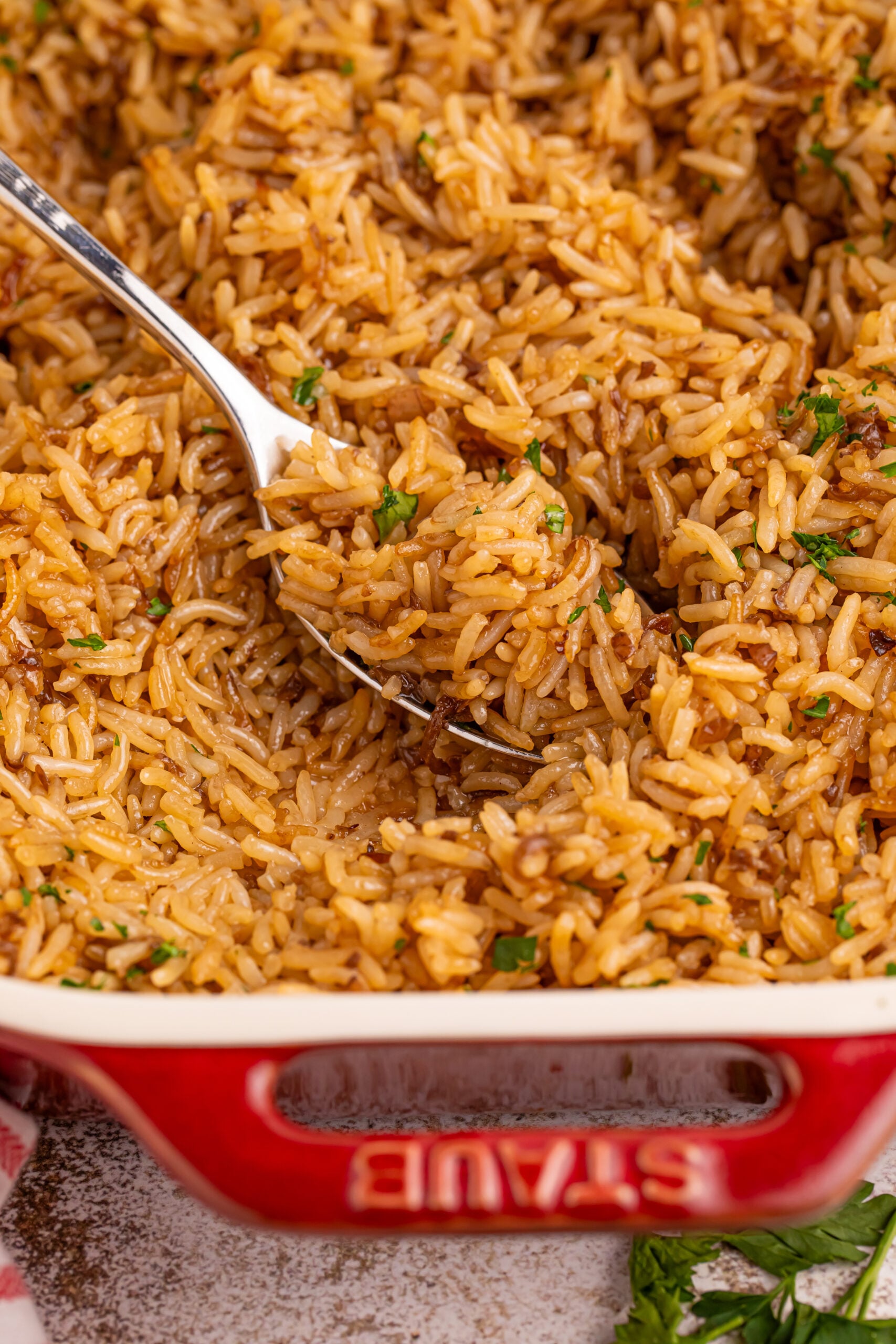 French Onion Soup Rice in a red baking dish with a spoon lifting up a bite