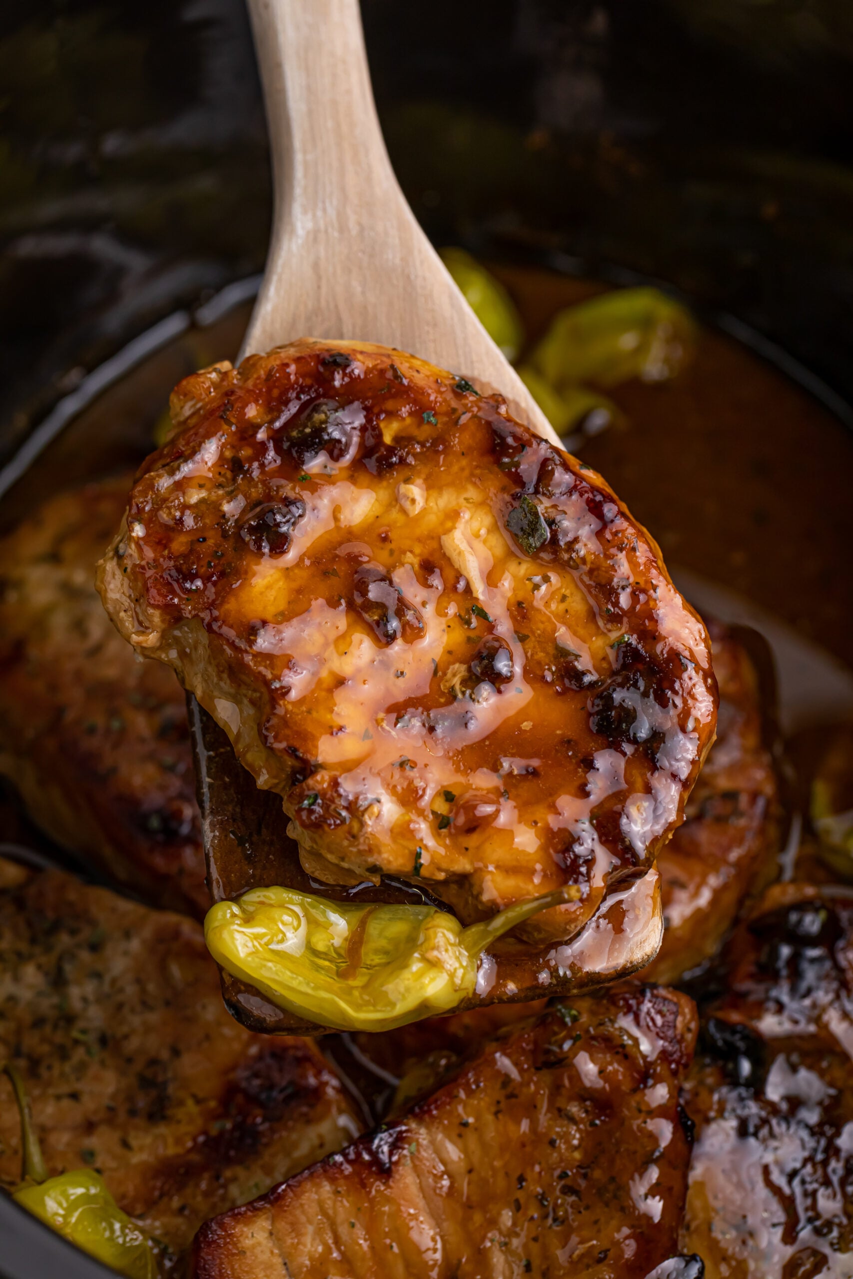 wooden spoon lifting a pork chop and pepper