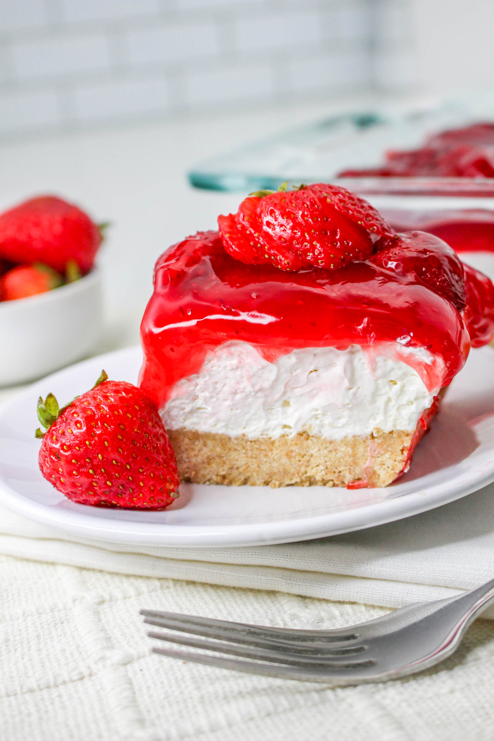Further away view of the No Bake Strawberry Delight on a white plate topped with sliced strawberries