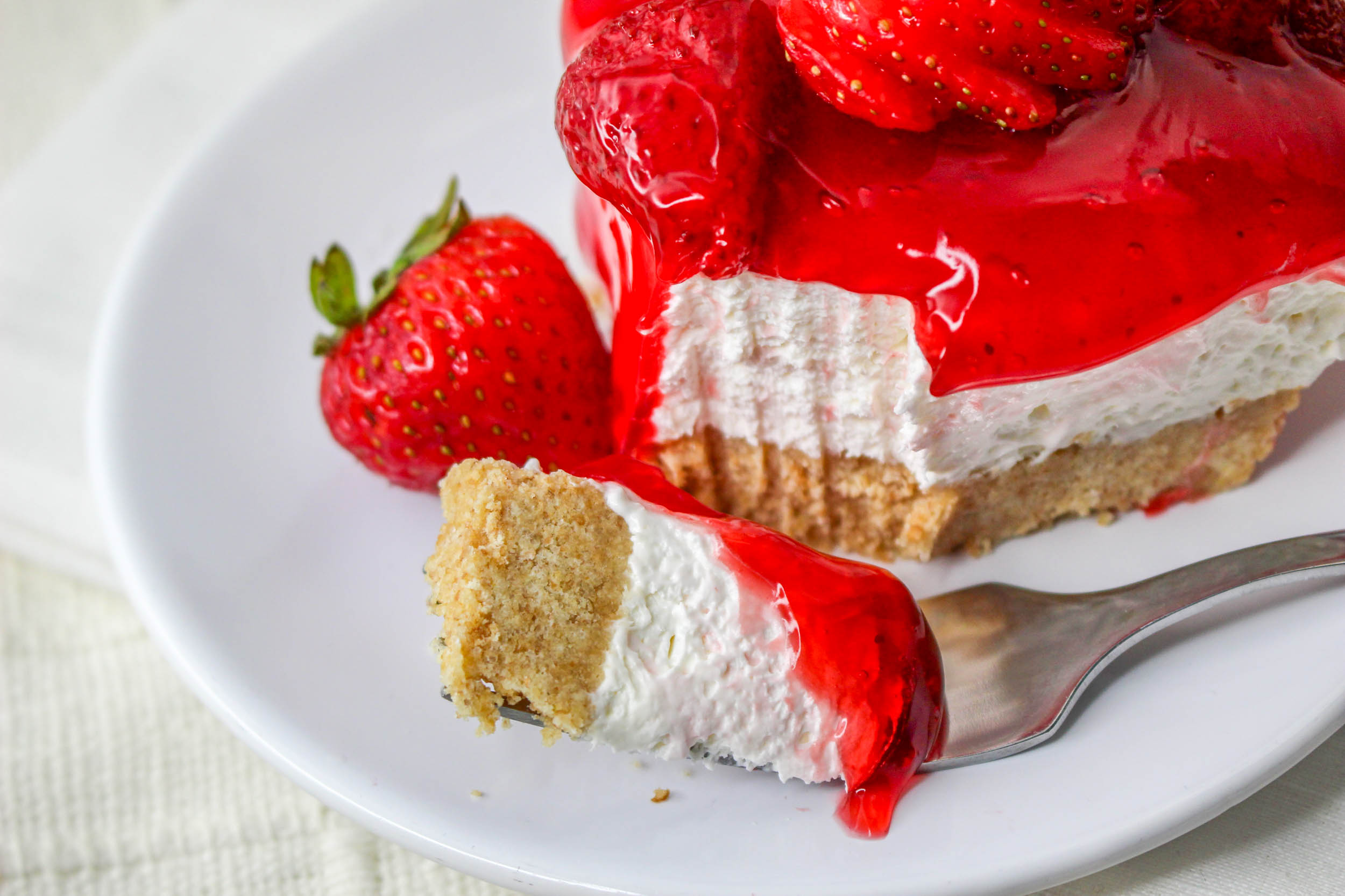 No Bake Strawberry Delight on a white plate with a bite missing topped with sliced strawberries