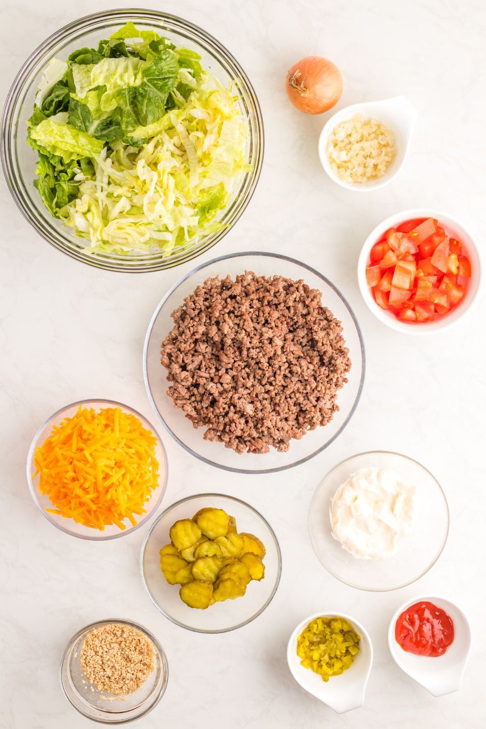 Big Mac Salad ingredients in bowls sitting on a white table 